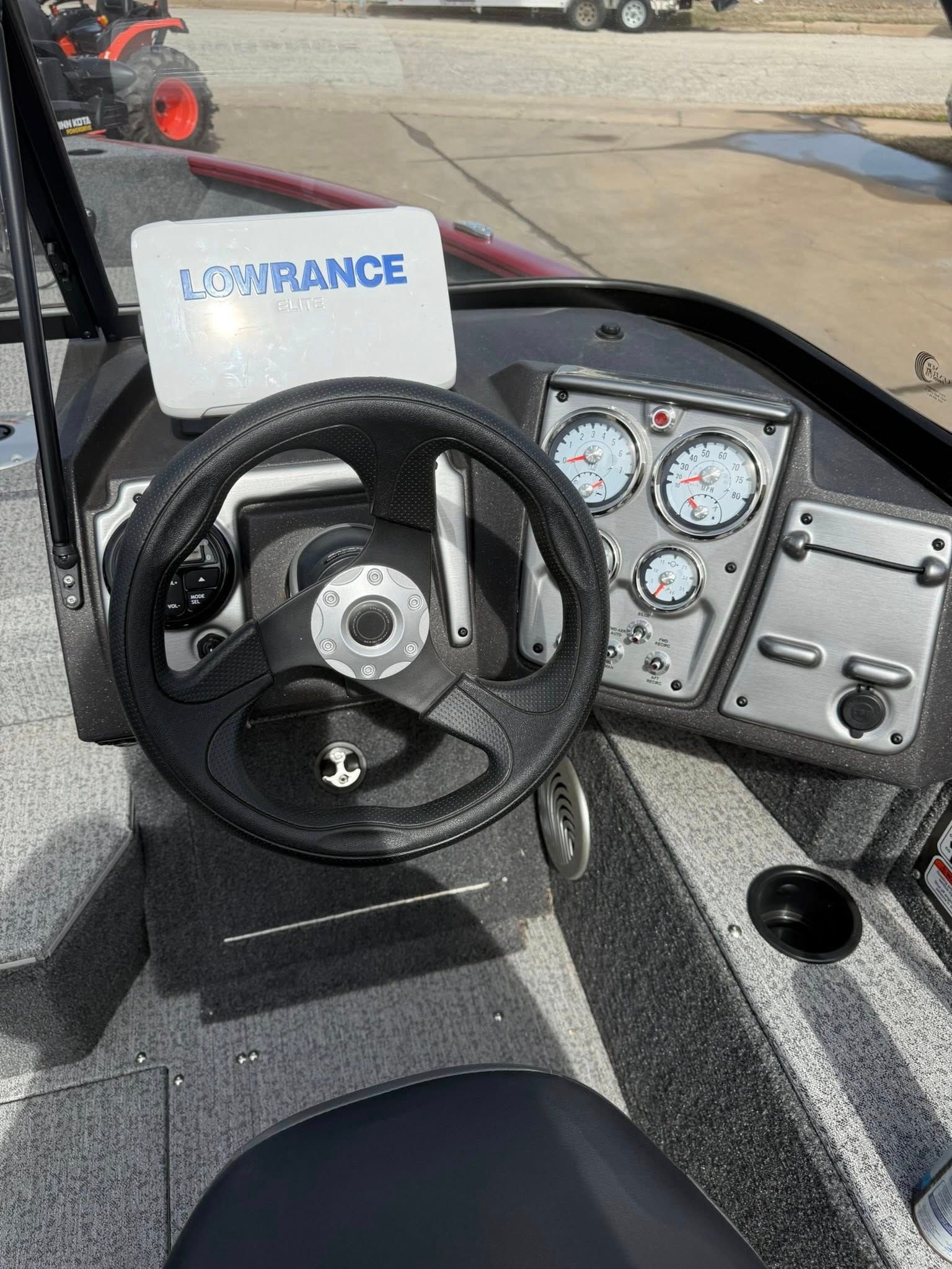 Boat helm with steering wheel, gauges, and throttle on a gray deck; “ENTRANCE” sign visible.