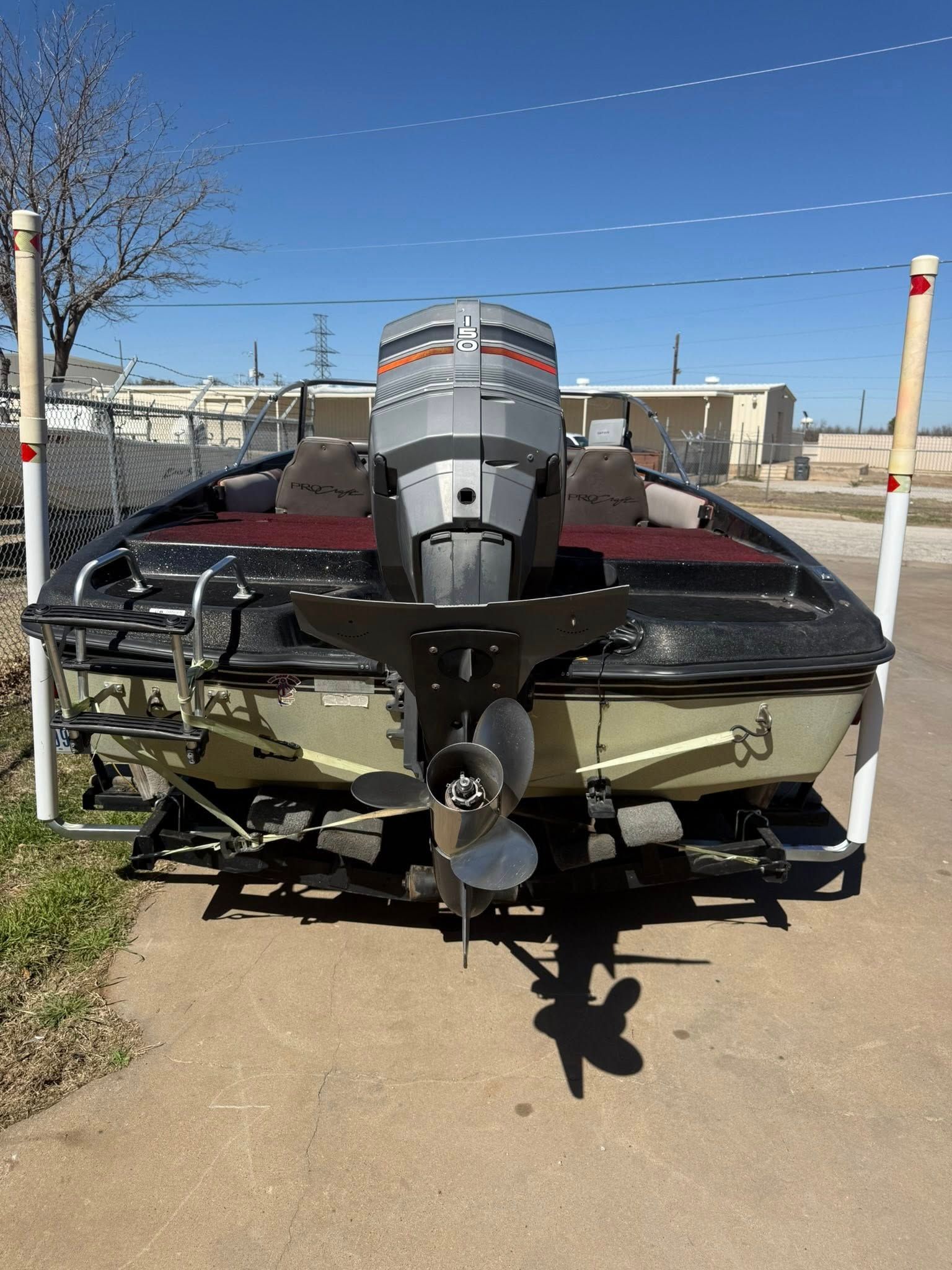 Small motorboat on a trailer, rear view with outboard engine, parked outdoors in a lot