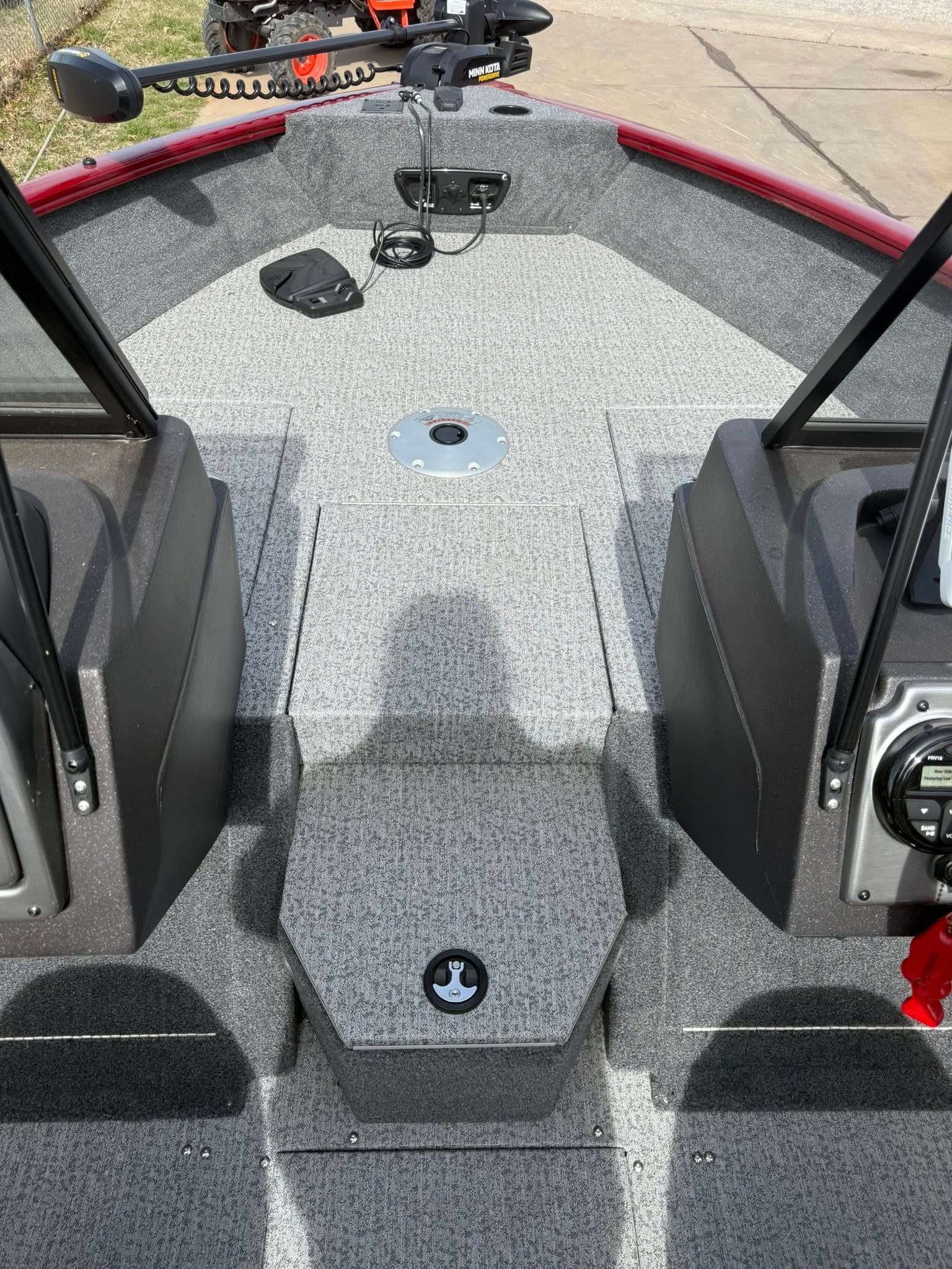 View from a small boat deck with rod holders, seats, and fishing gear on a gray carpeted floor.