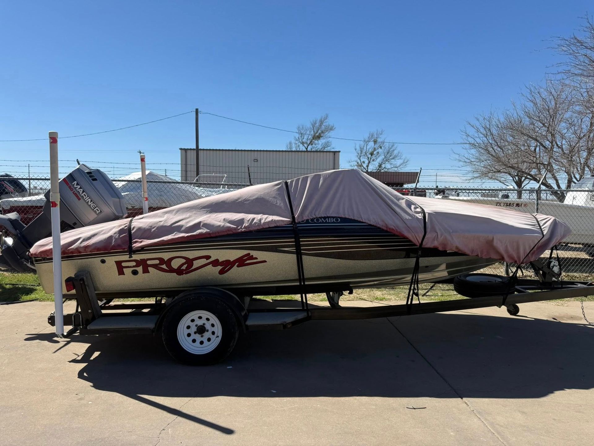 Covered boat on trailer in a parking lot under a clear blue sky.
