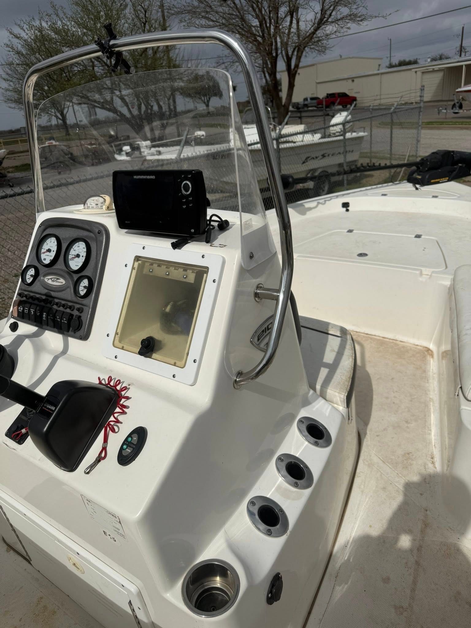 White boat helm console with gauges, controls, and a clear windshield on a docked boat.
