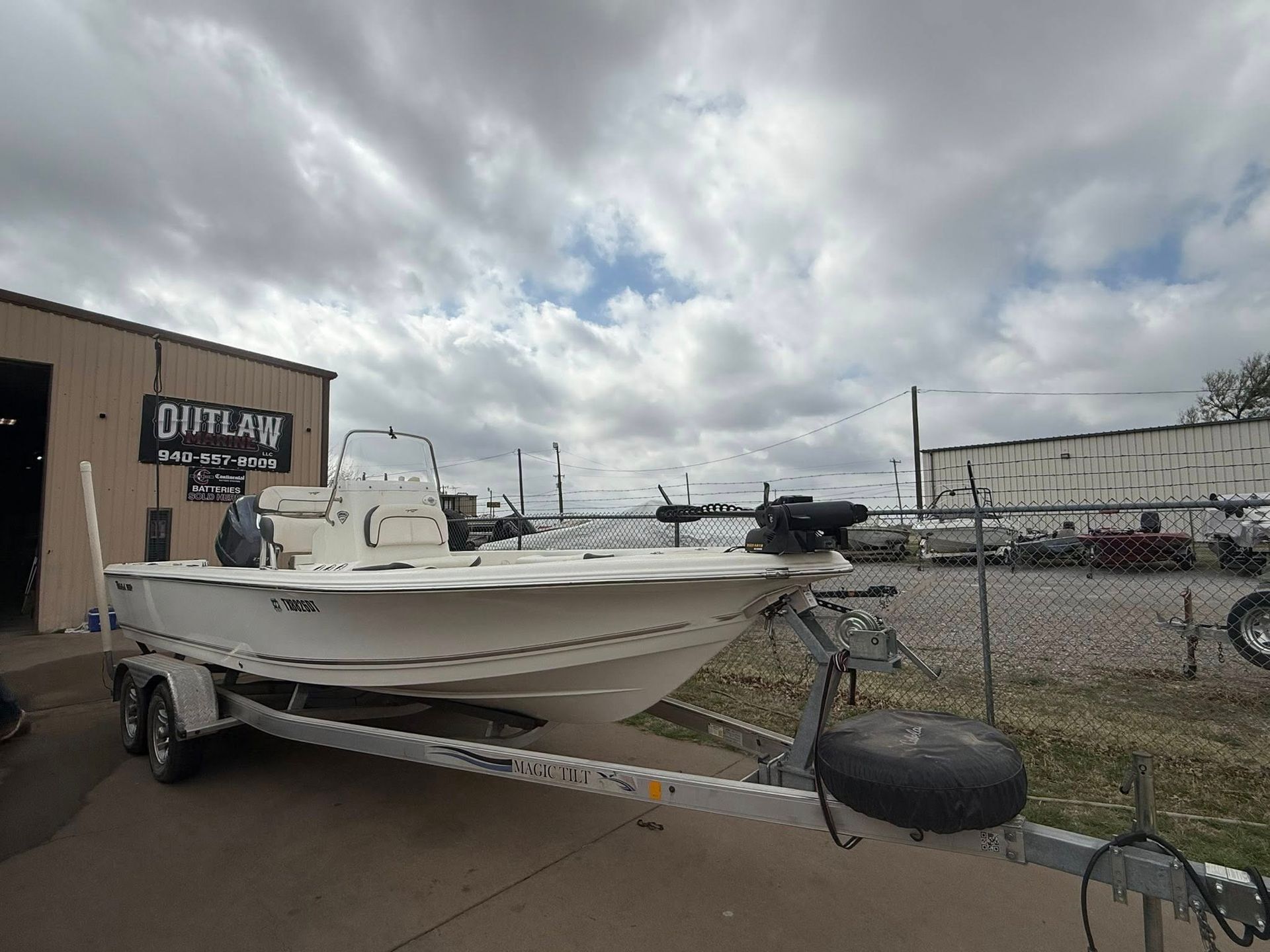 White boat on a trailer beside a building and fence under a cloudy sky
