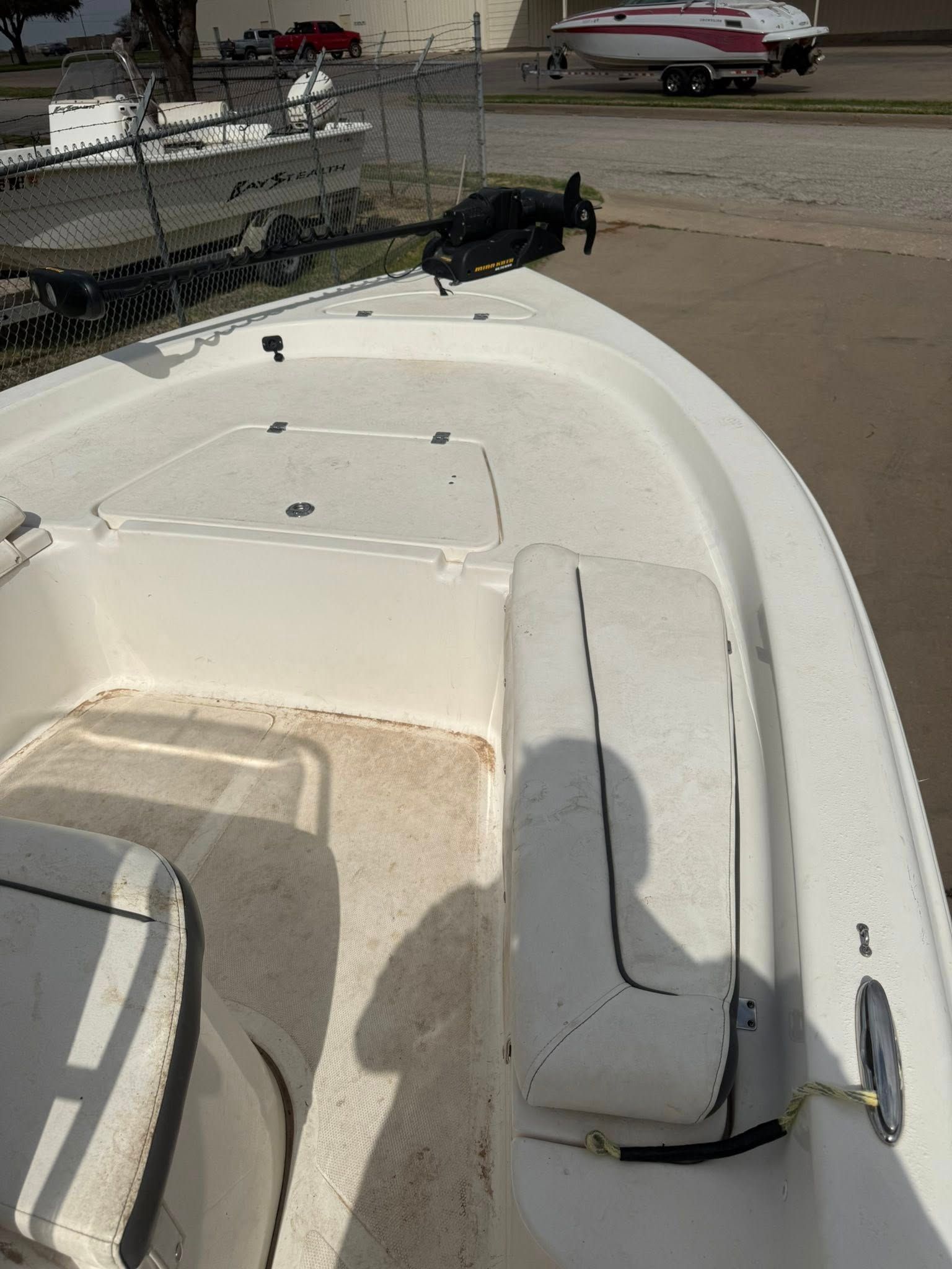 White boat deck with cushioned seats at a marina, with boats and water in the background