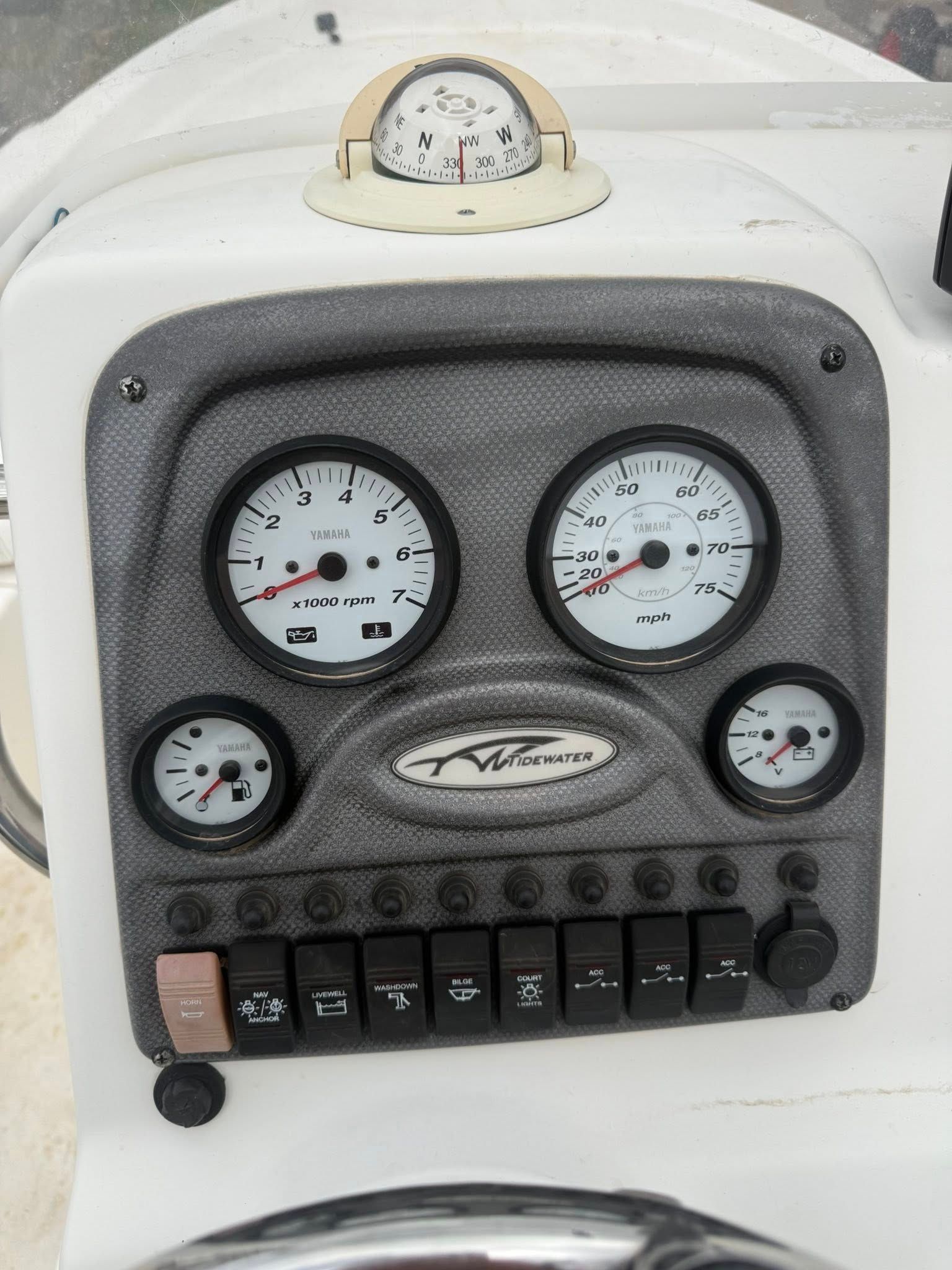 Gray marine dashboard with multiple round gauges, switches, and a central logo on a white boat console