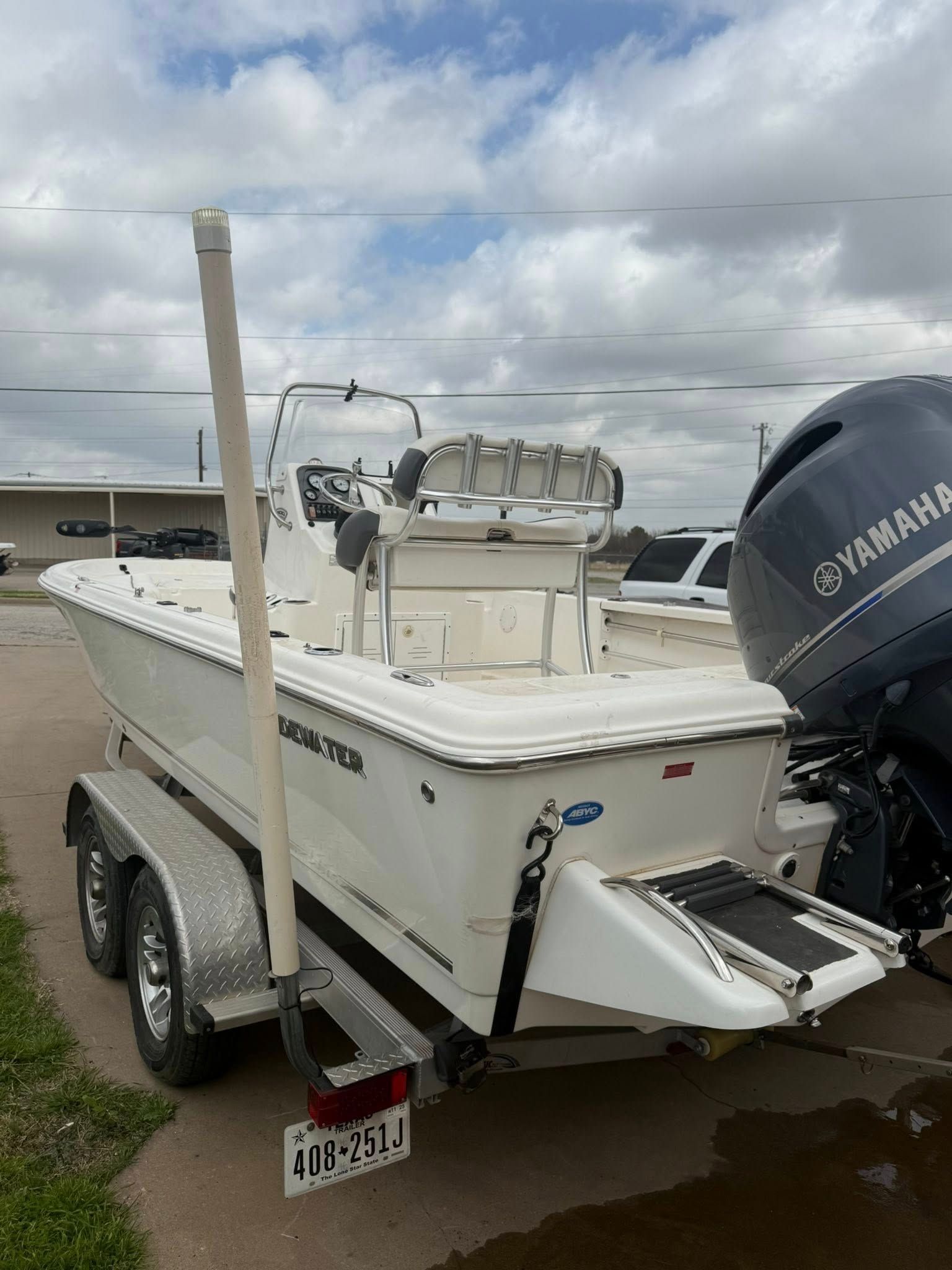 White motorboat on a trailer with a Yamaha outboard, parked on a gravel lot under cloudy skies.