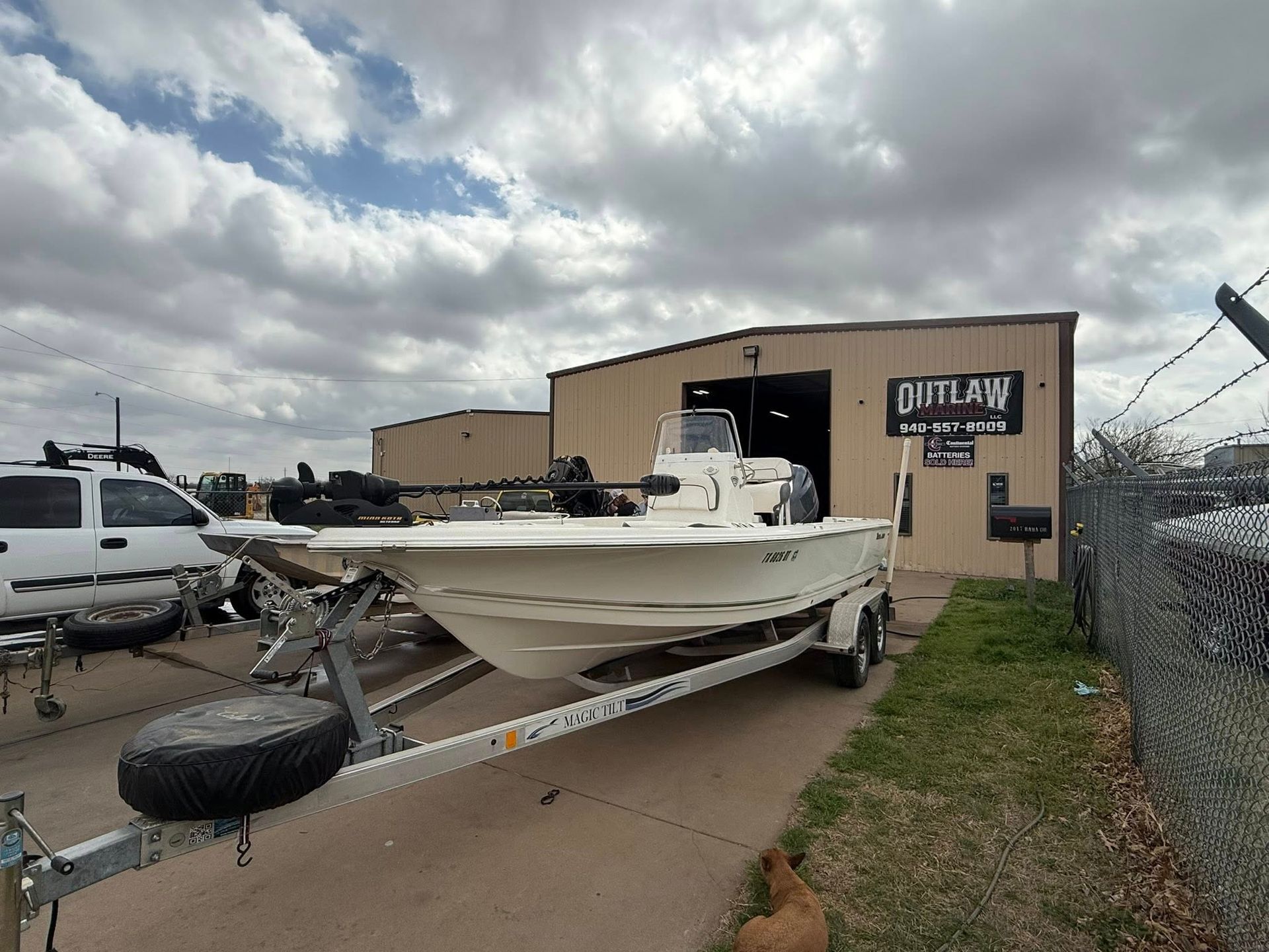 White fishing boat on a trailer outside a beige building under cloudy skies