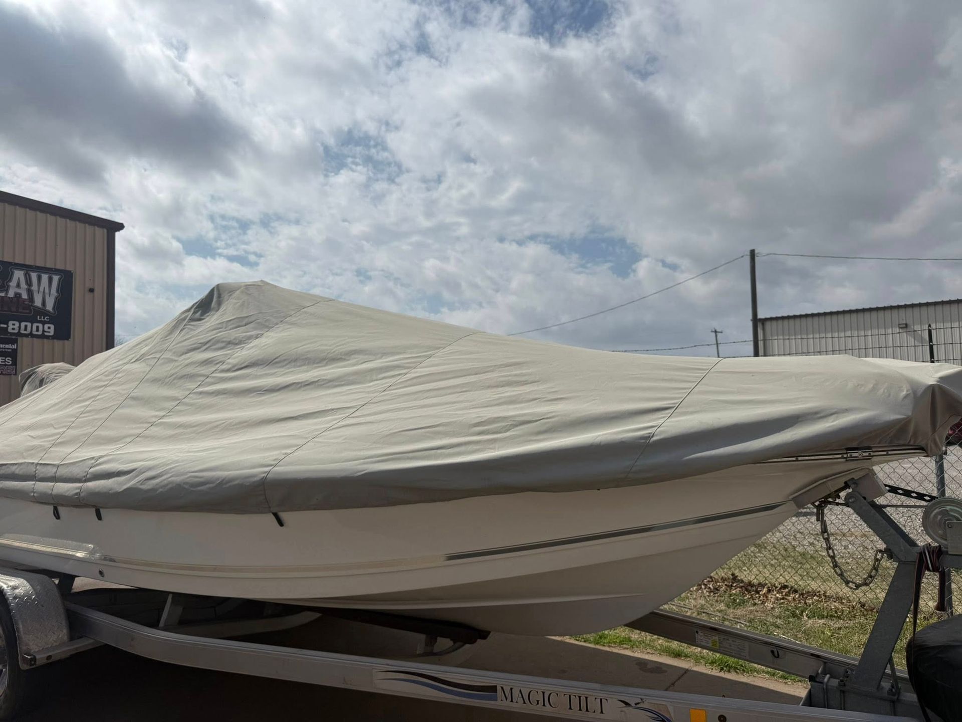 Boat covered with a gray tarp on a trailer under a cloudy sky
