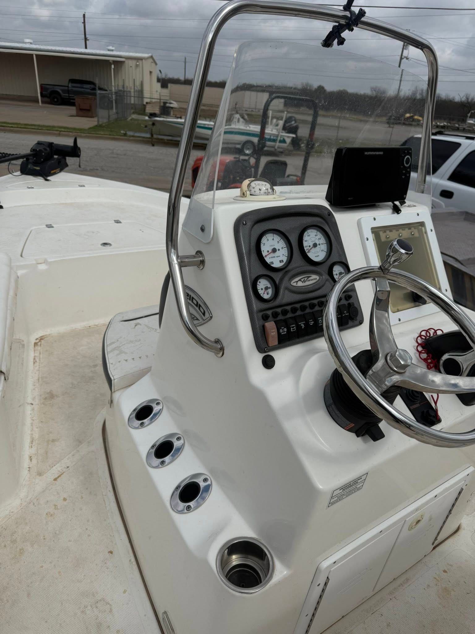 Boat helm with gauges, steering wheel, and rod holders on a white center-console boat at a marina.