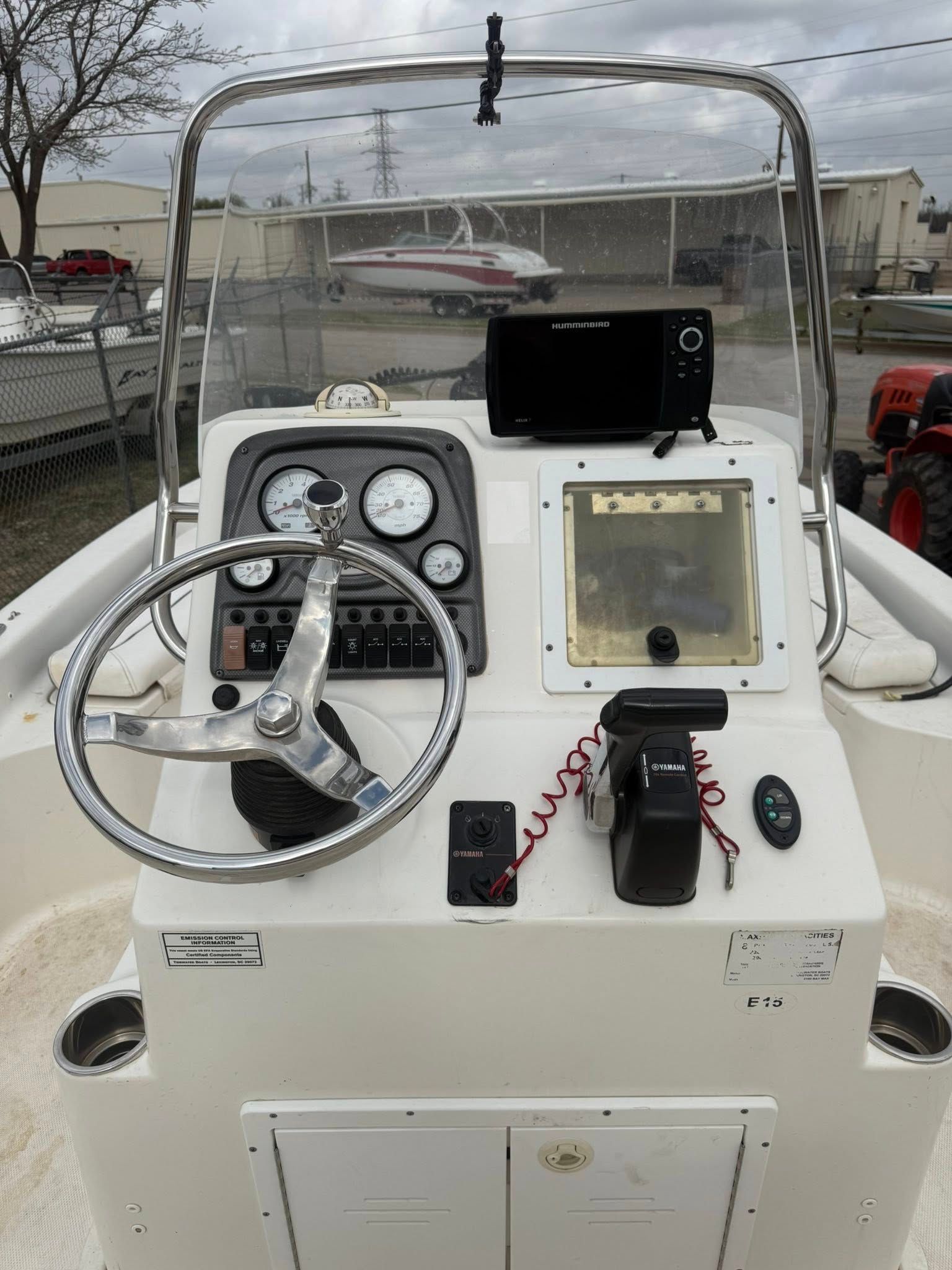 Boat helm with steering wheel, gauges, and throttle on a white console at a marina.