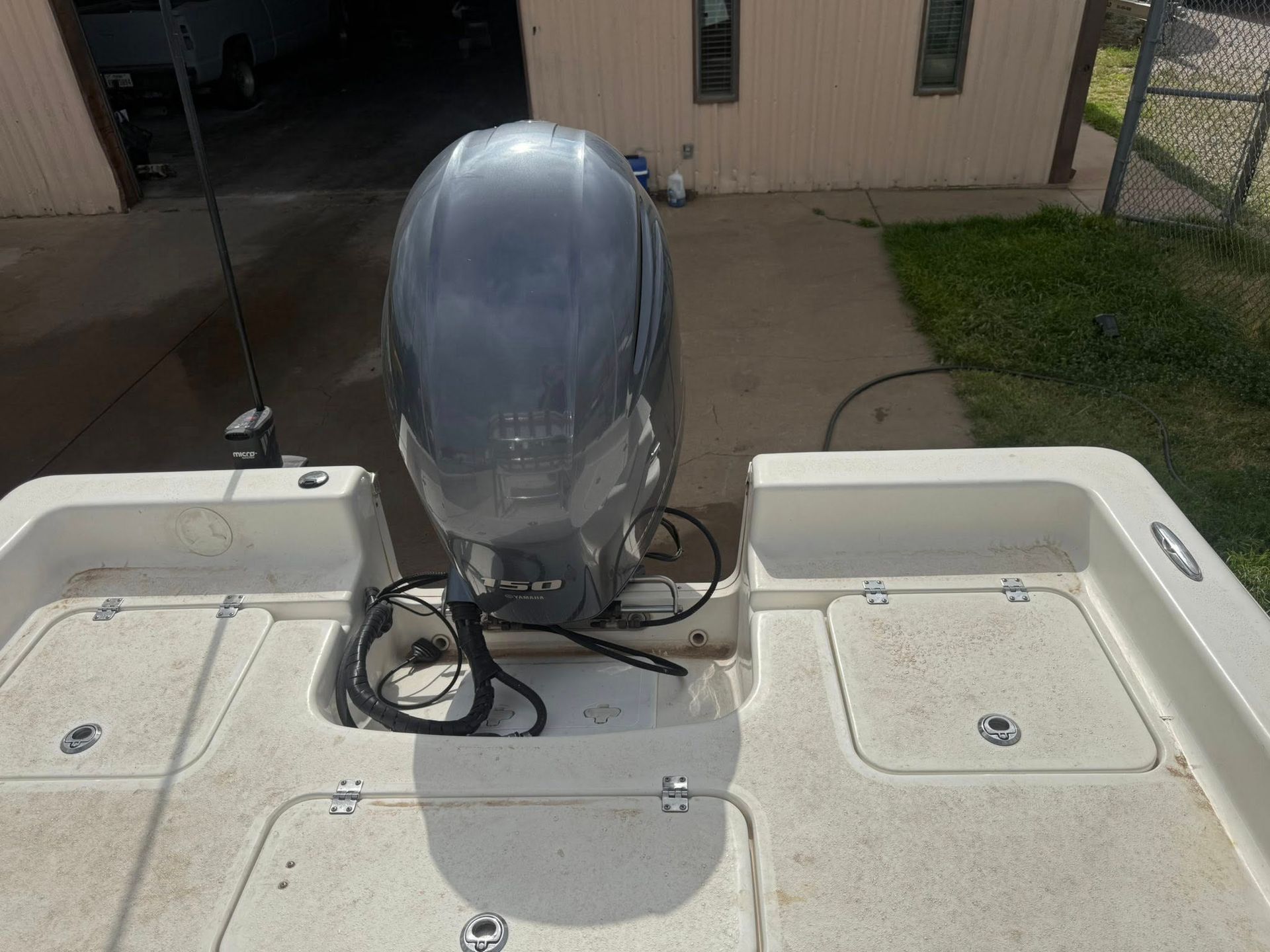 Boat stern with outboard motor on a dock, with two white hatches and a house in the background