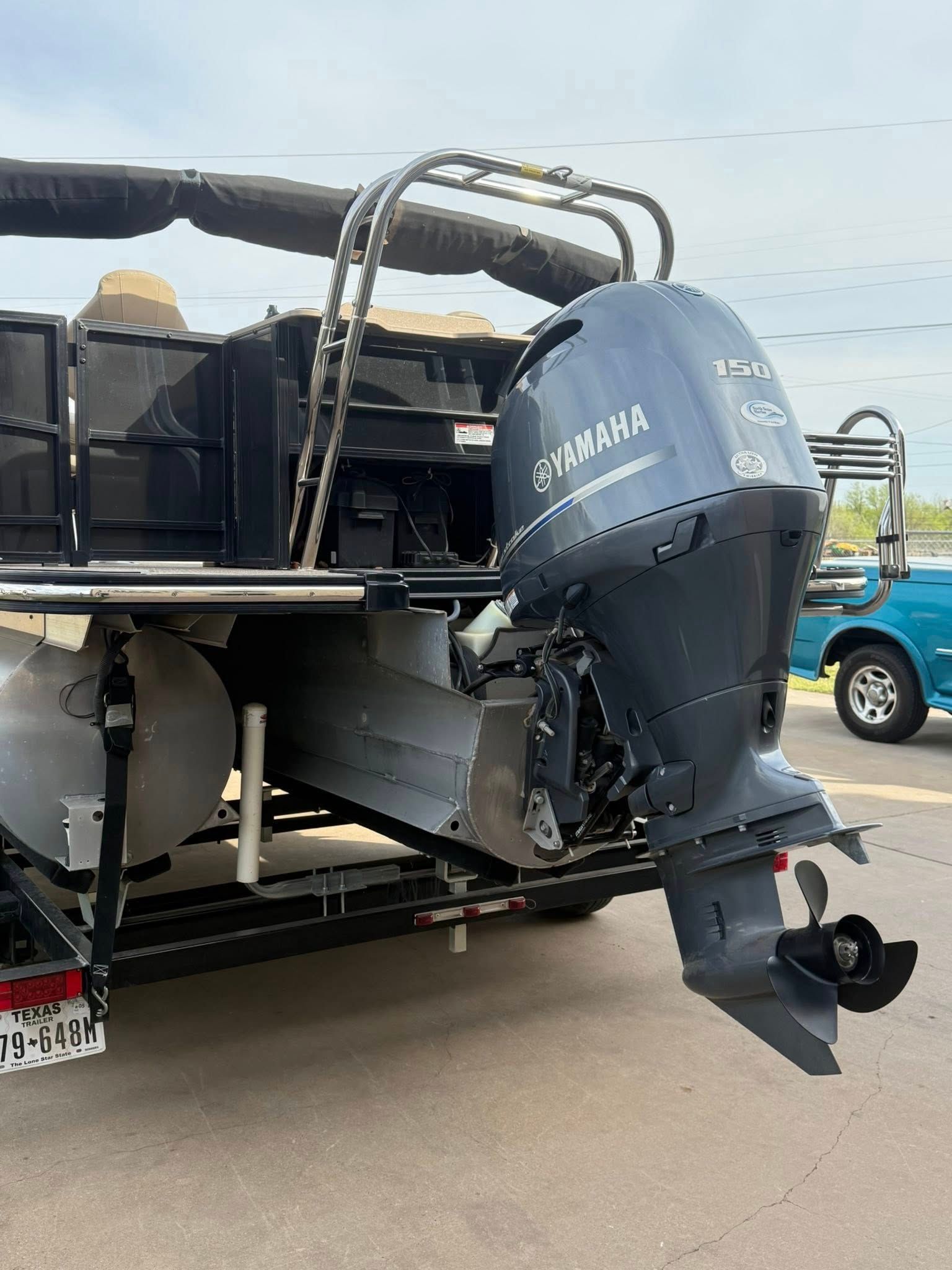 Black pontoon boat with a Yamaha outboard motor parked on a trailer in a lot