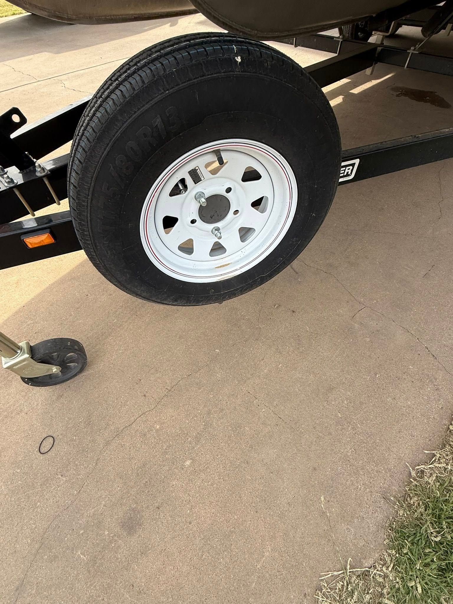 Trailer wheel with white rim on black frame, parked on pavement near grass