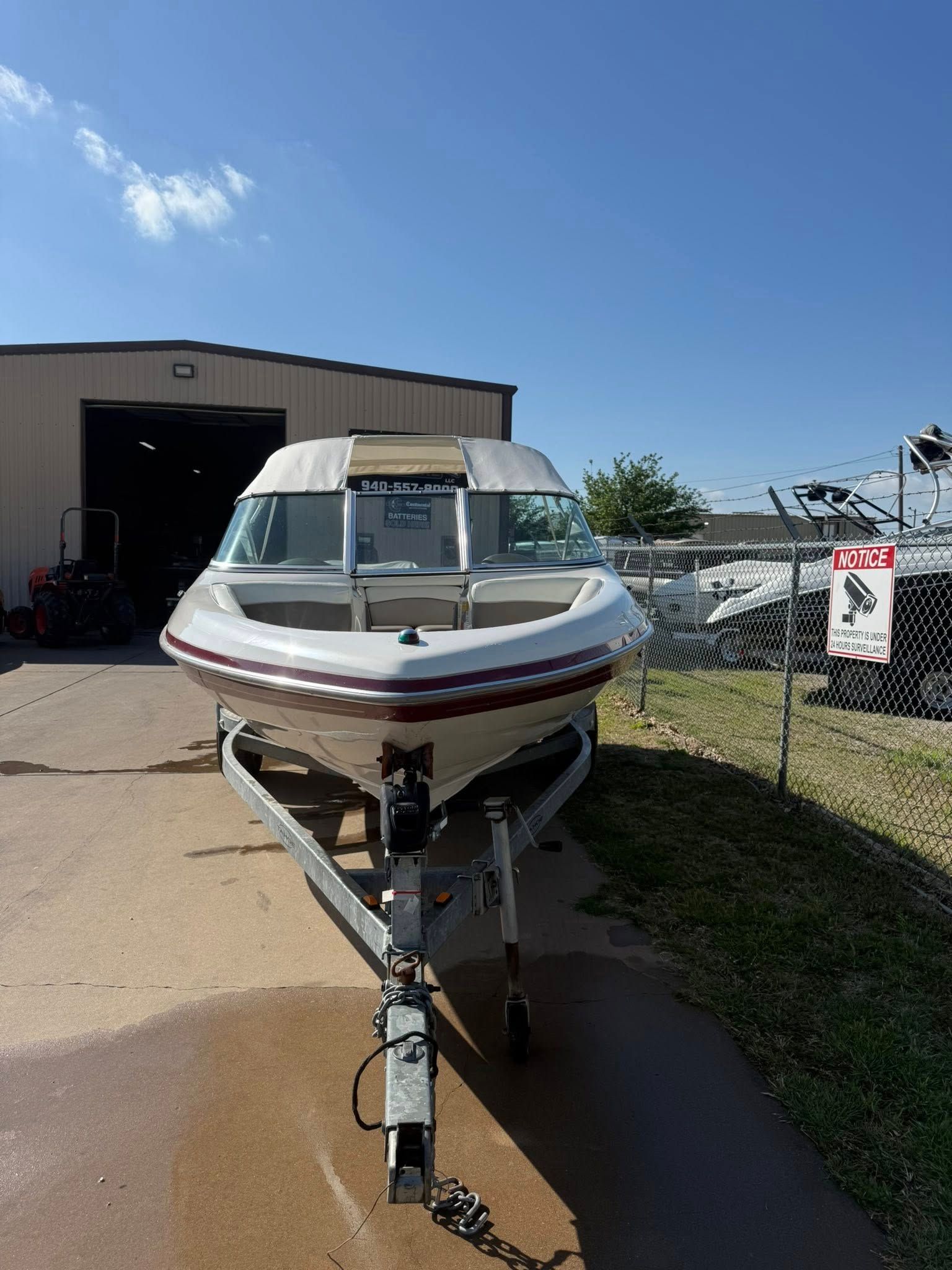 White motorboat on a trailer in a lot outside a boat storage building under a clear blue sky