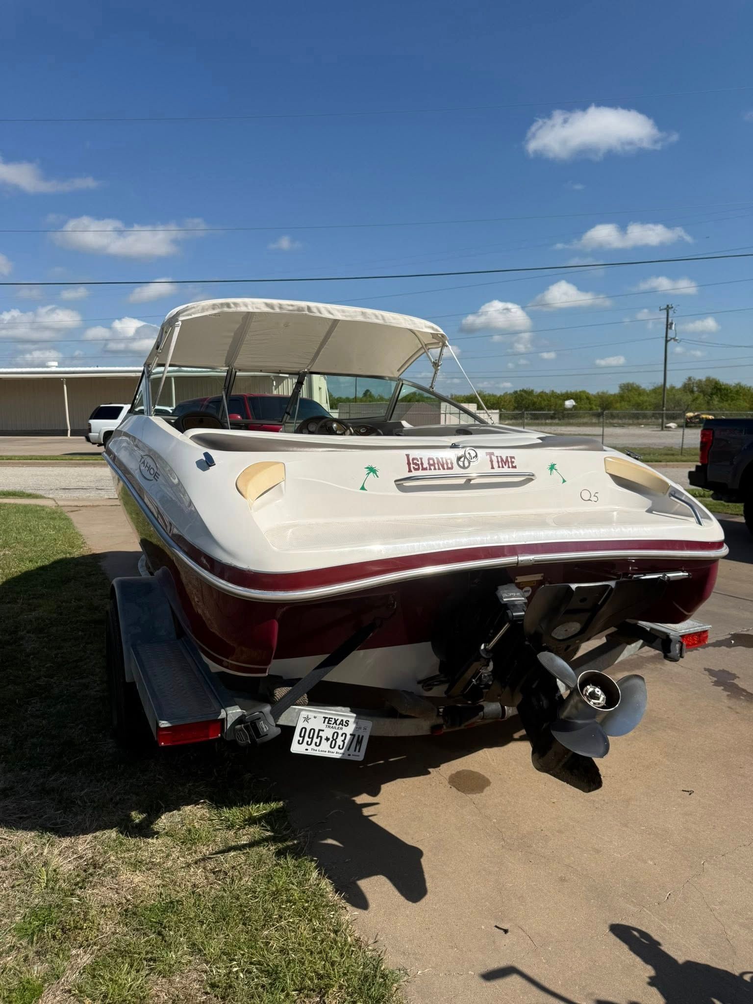 White and maroon speedboat on a trailer parked outdoors under a blue sky