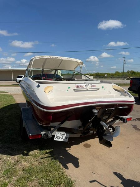 White and burgundy speedboat on a trailer in a parking lot under a blue sky
