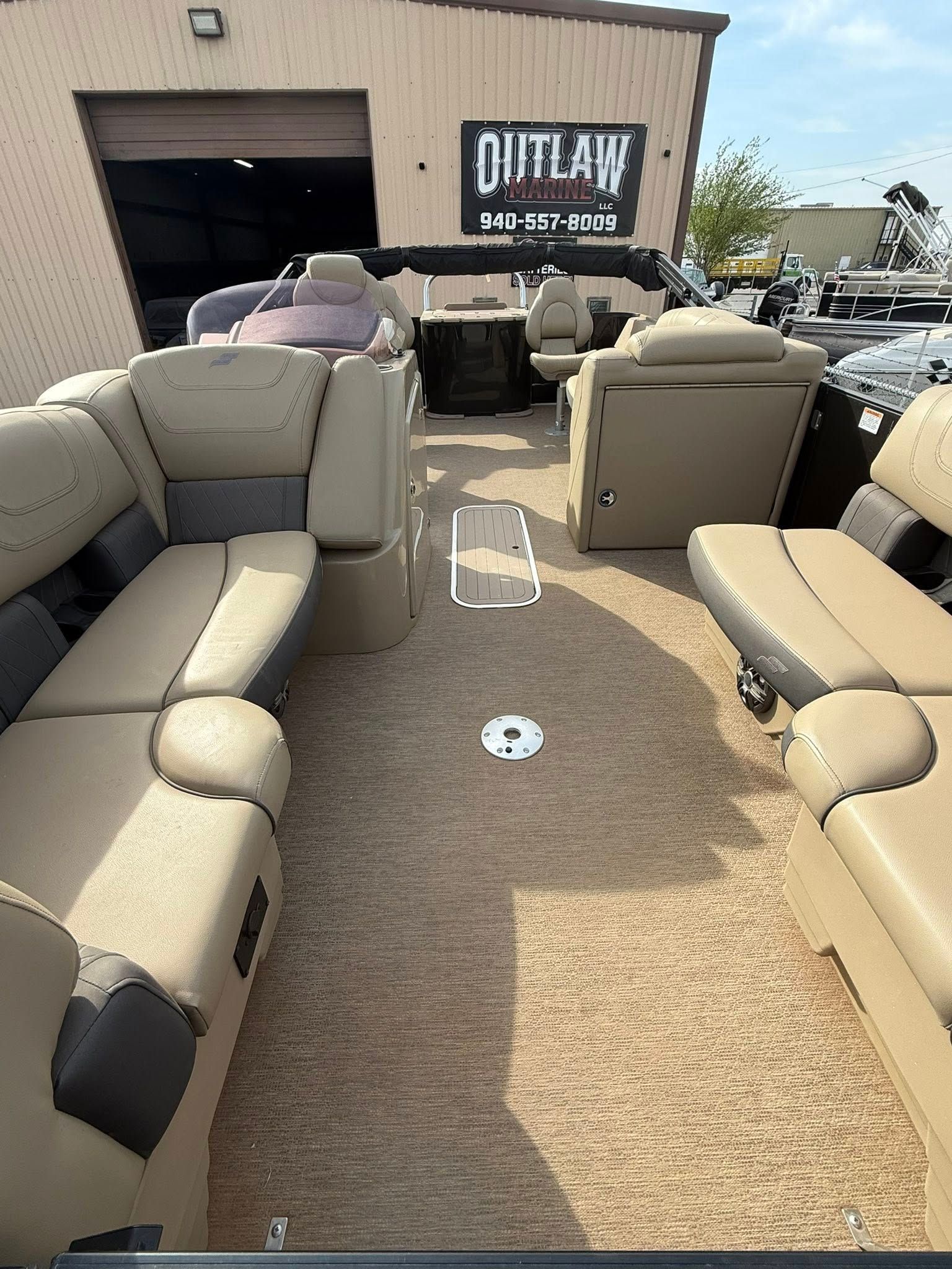 Outdoor furniture display with beige recliner seats arranged around a carpet sample in front of a warehouse.
