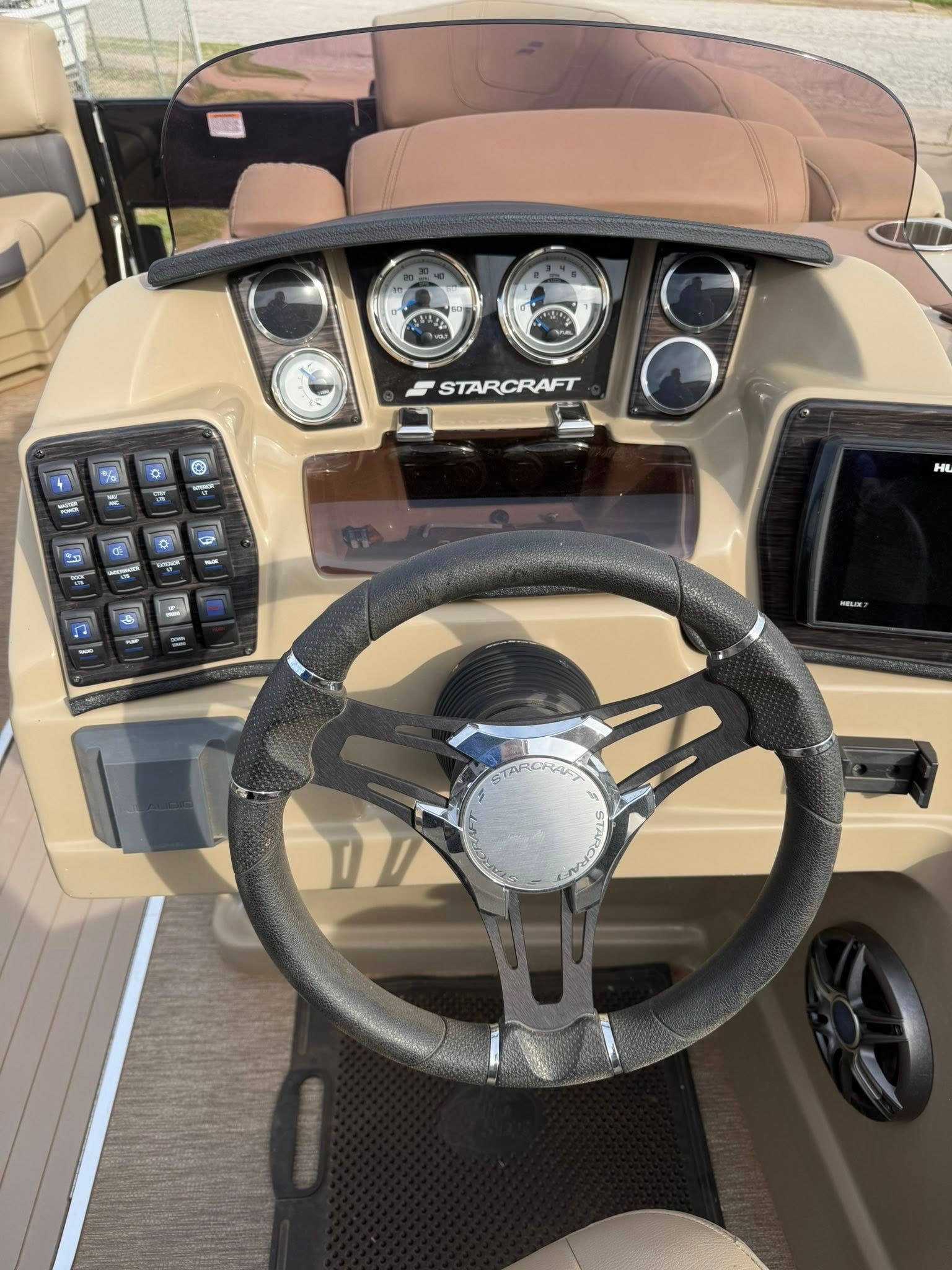 Boat cockpit with tan seats, black steering wheel, and dashboard gauges and controls
