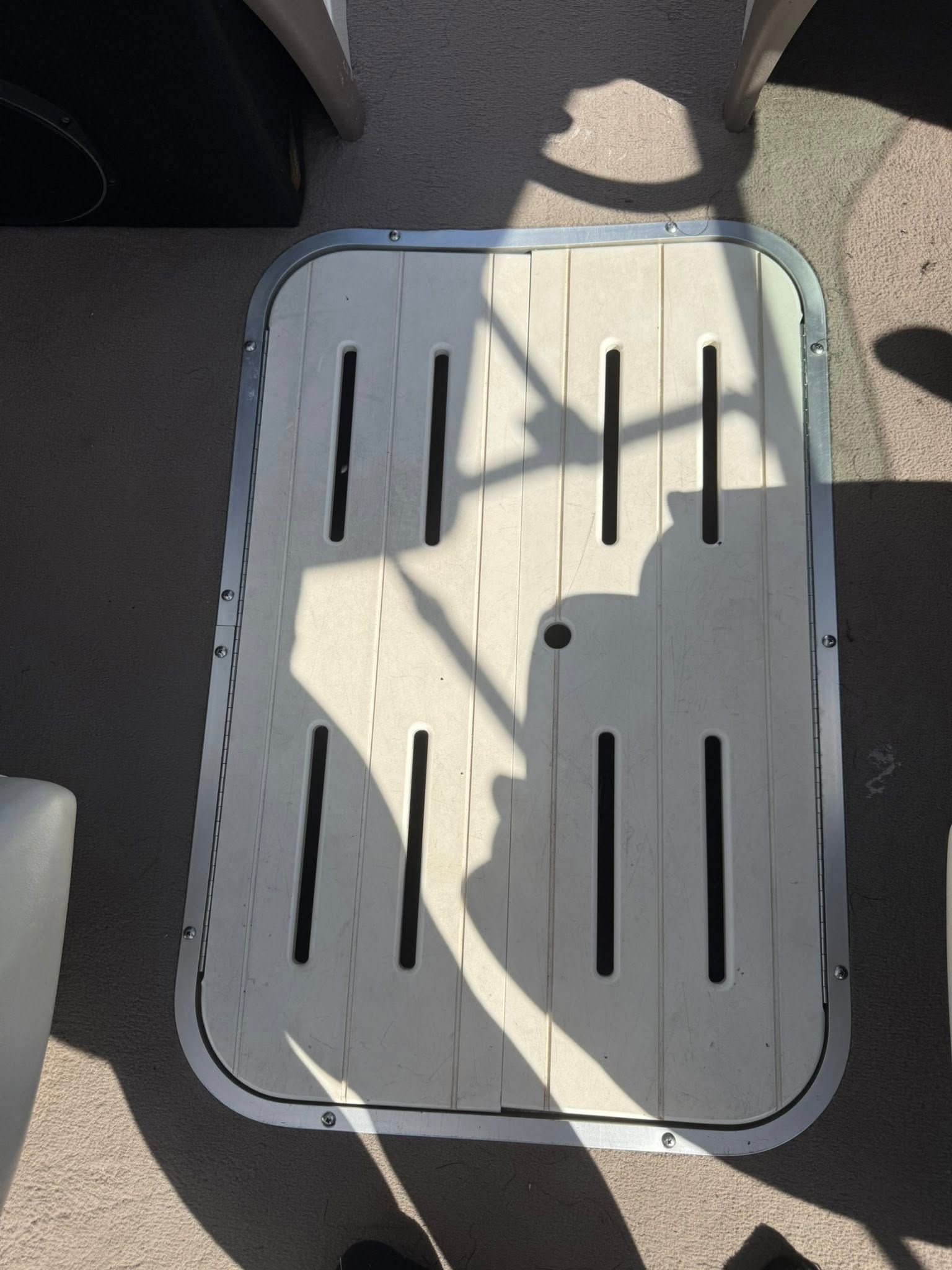 White rectangular hatch cover with black slots on a sunlit outdoor floor.