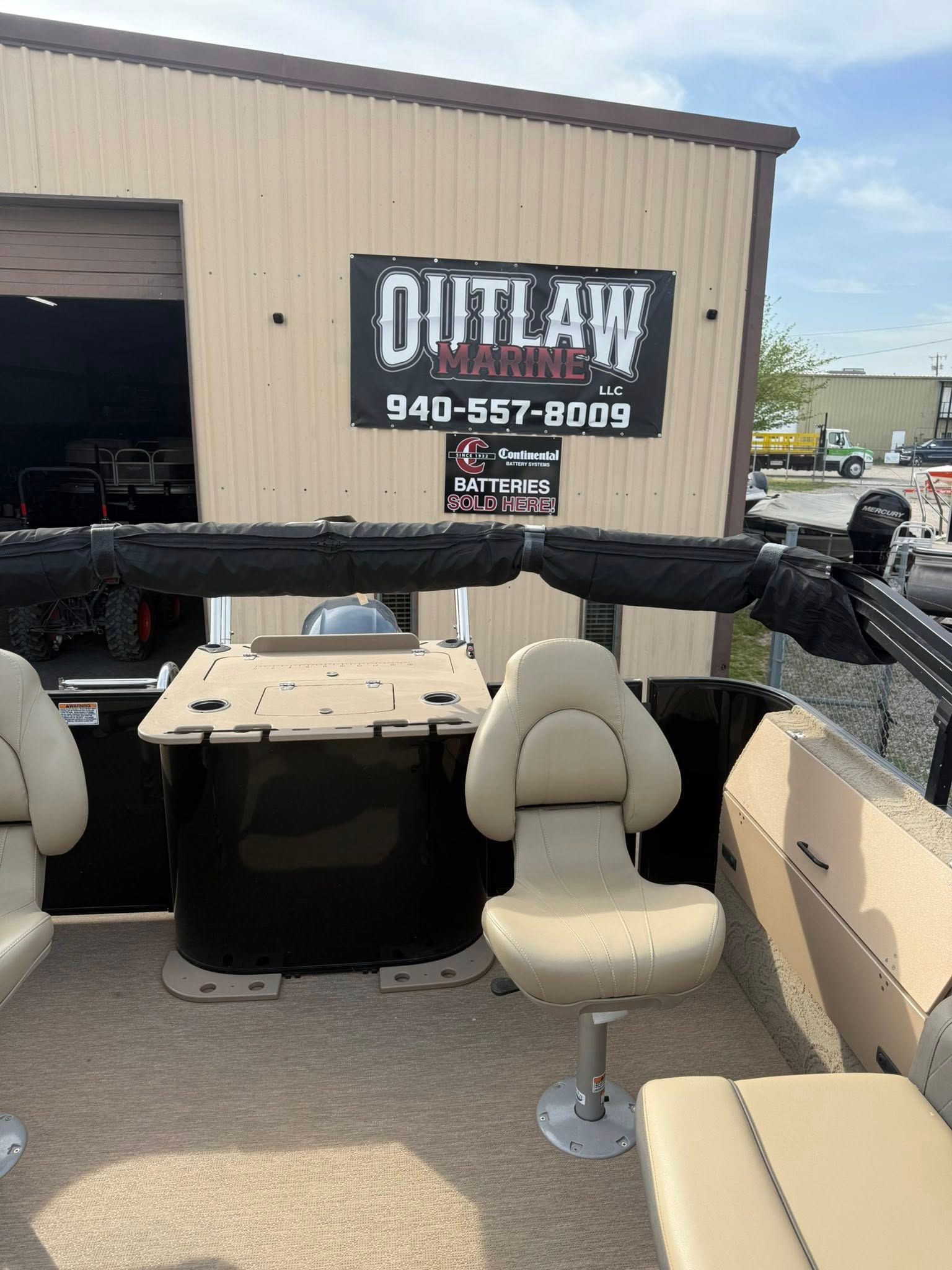Open boat interior with beige seats in front of an Outlaw fence sign outside a shop.