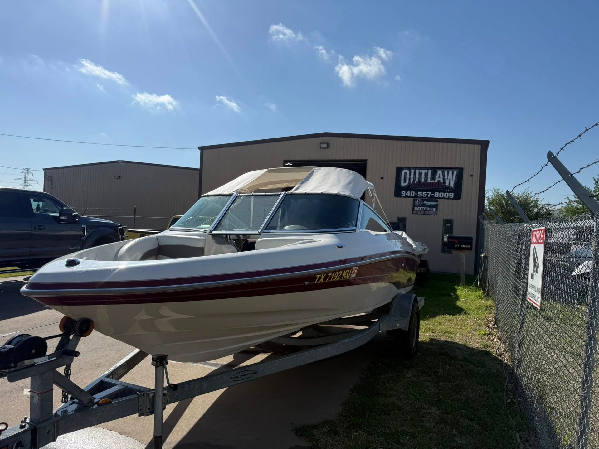 White speedboat on a trailer outside a boat dealership, with a blue sky overhead