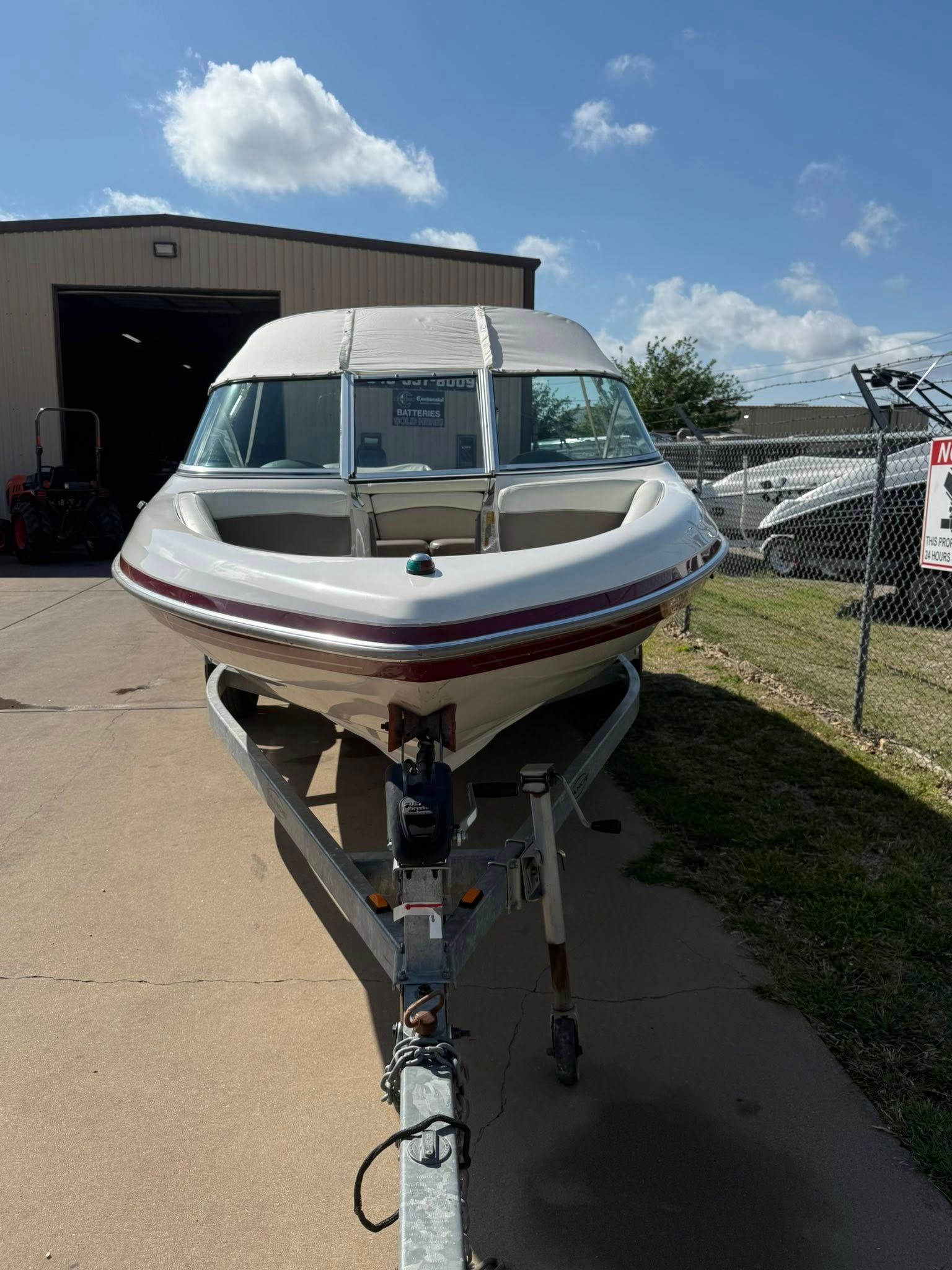 White and maroon motorboat on trailer outside a boat storage building under a blue sky