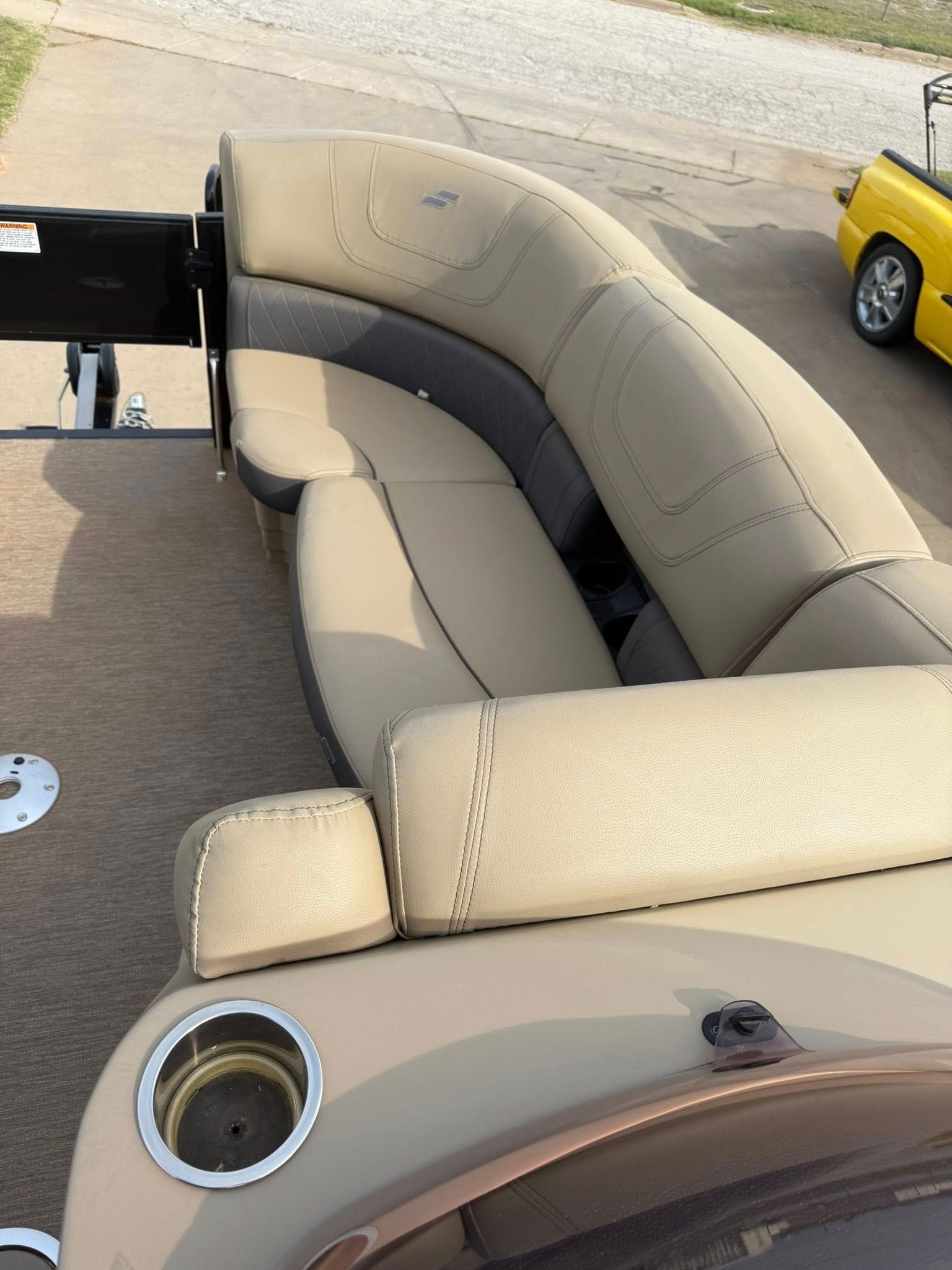 Beige curved seating on a boat or patio with a cup holder, beside a black seat and yellow vehicle