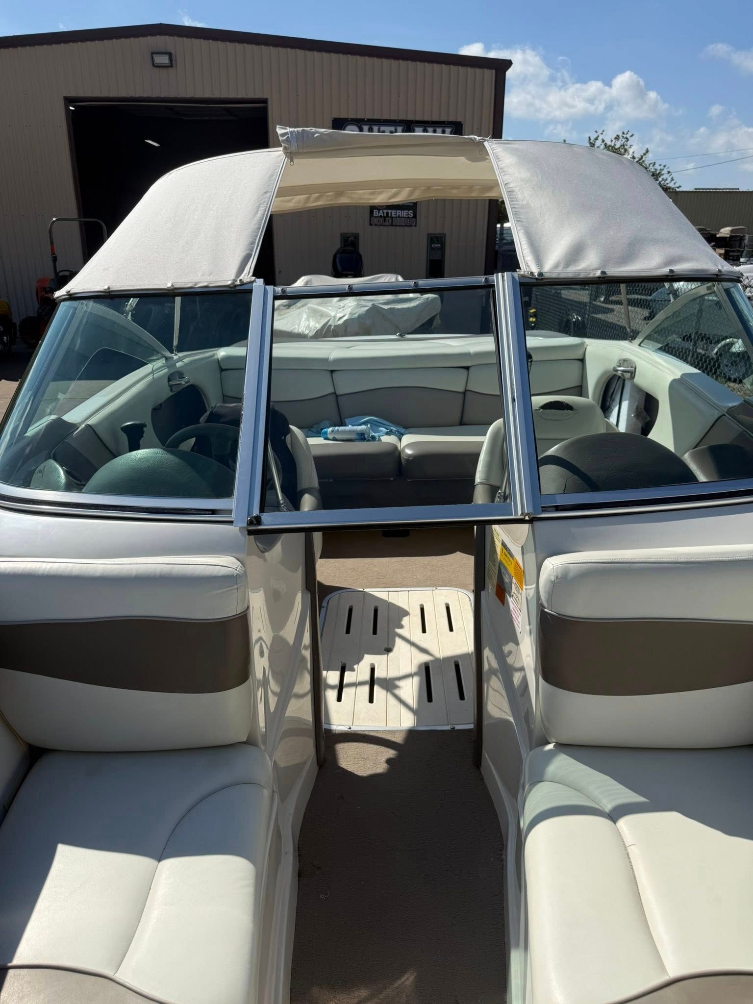 Interior of a white boat with two front seats and a center walkway, parked near a boathouse under a canopy.