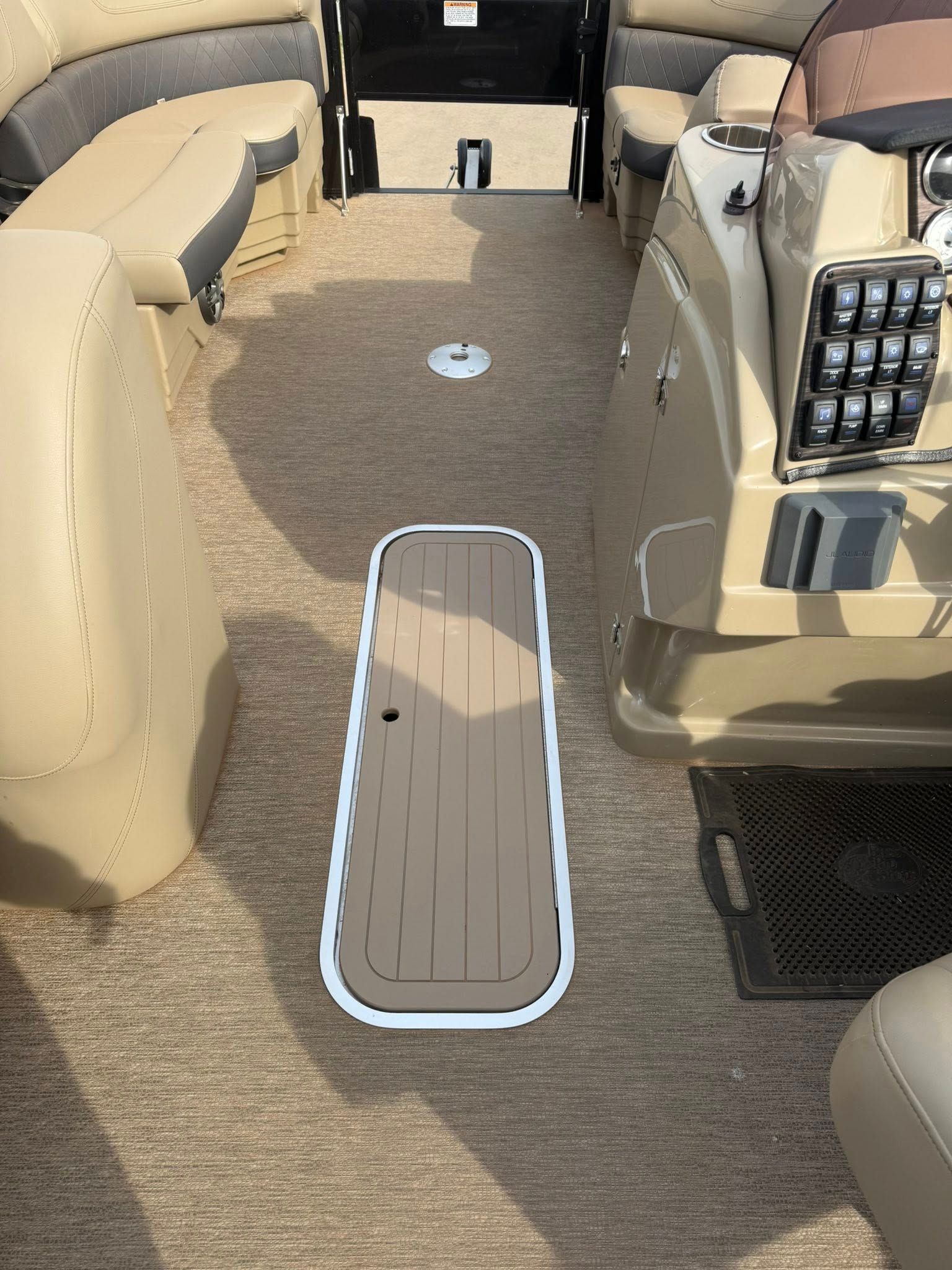 Boat cabin walkway with beige seats and a highlighted floor hatch panel centered on the carpeted floor.