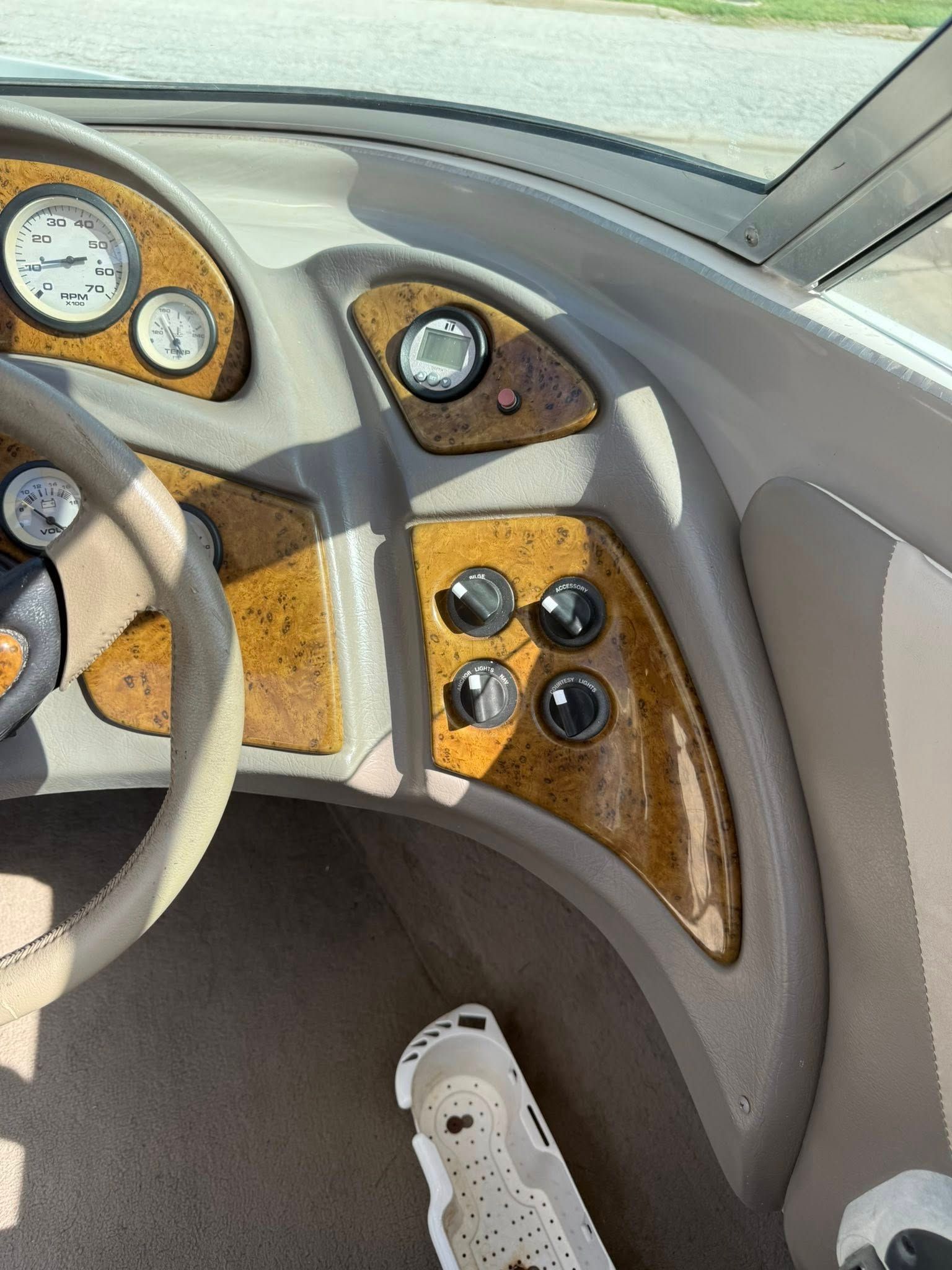 Boat cockpit with tan and woodgrain dashboard, round gauges, and a white shoe visible below