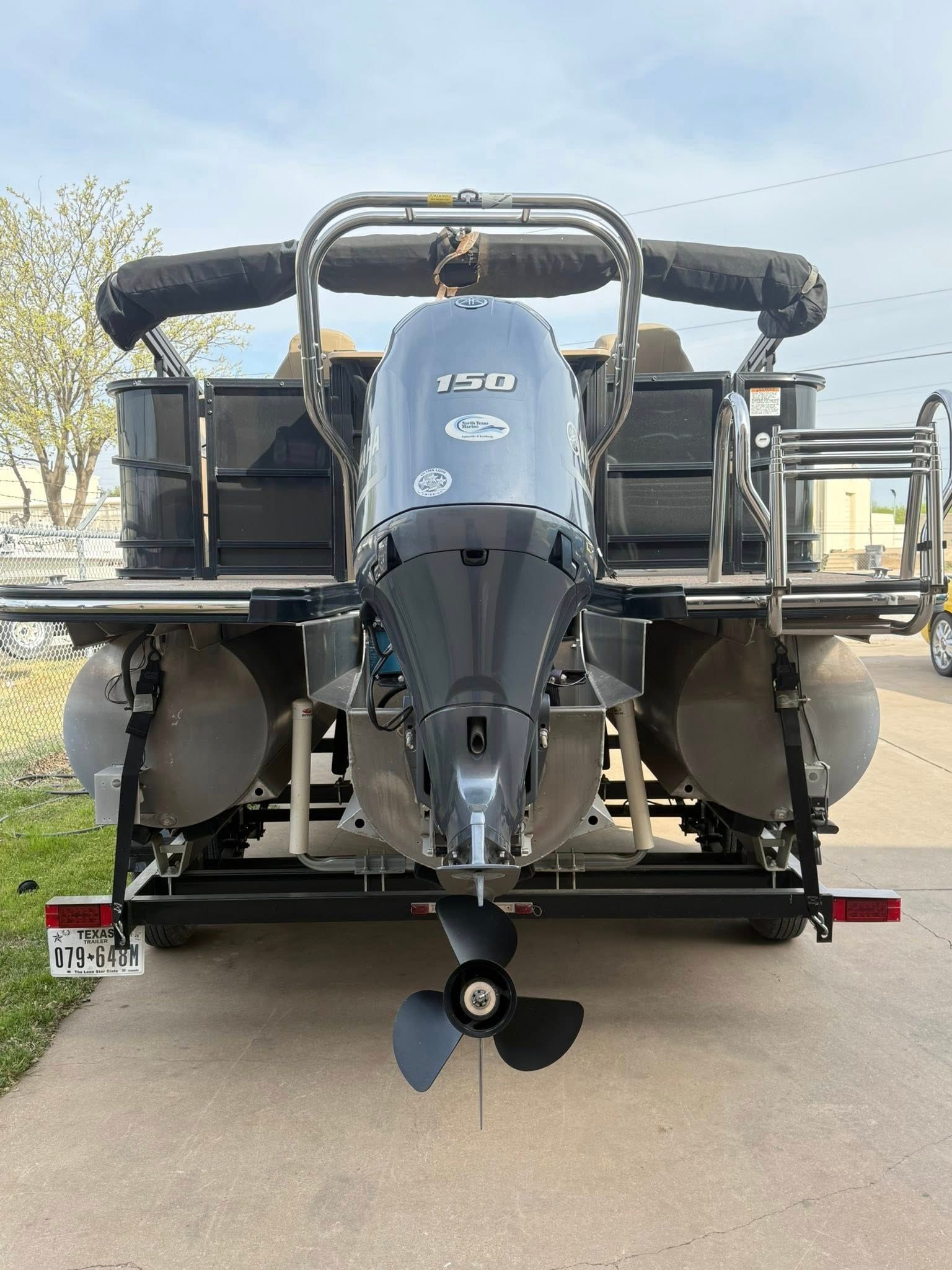 Rear view of a small motorboat on a trailer, with outboard engines and a black propeller on a paved lot