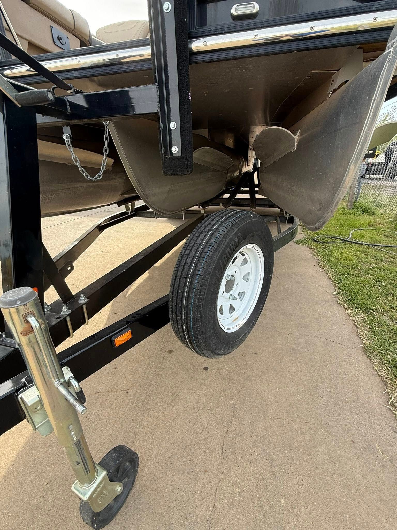 Close-up of a boat trailer with a white wheel, black frame, and metal hitch parked on a concrete path.