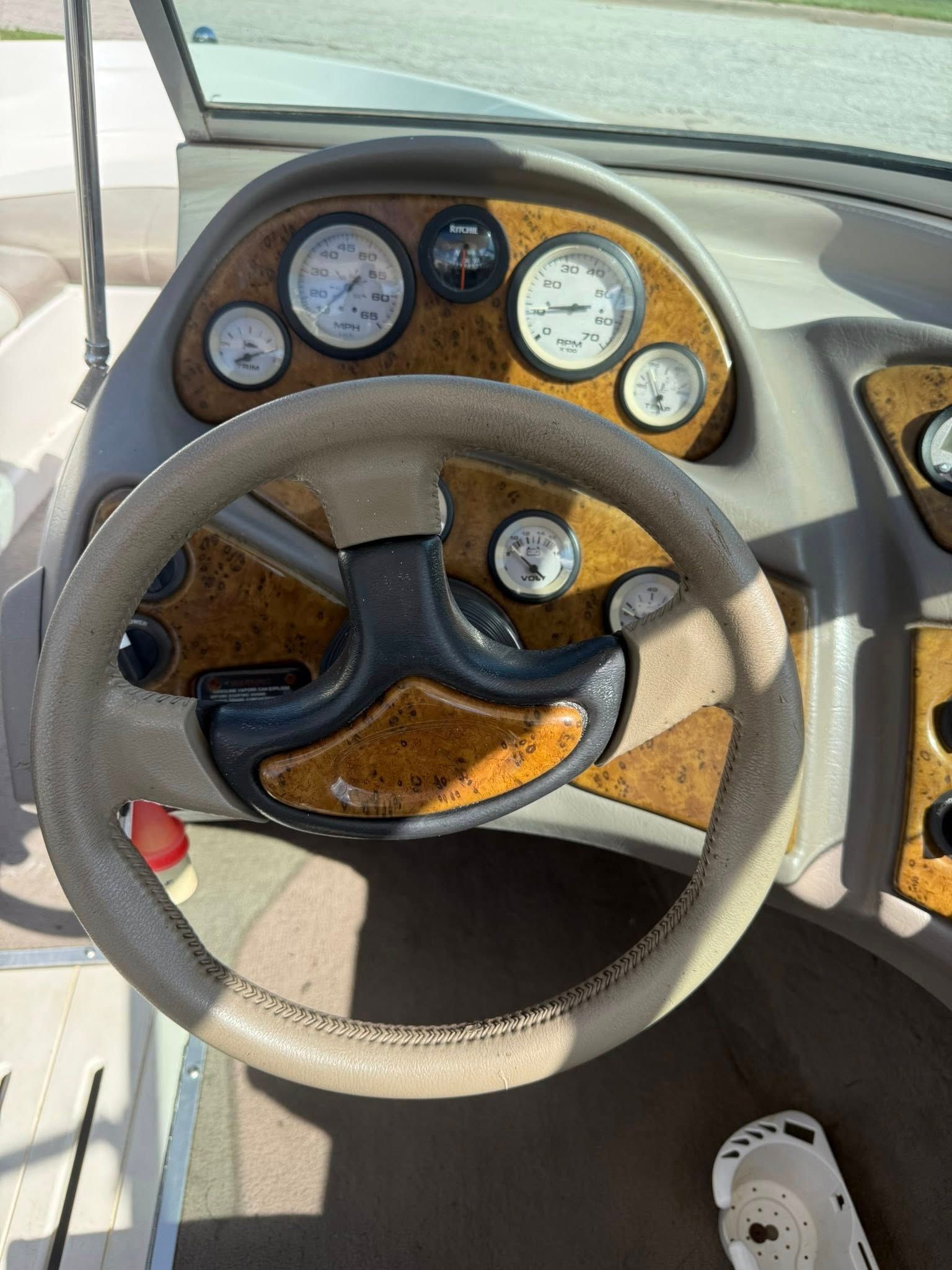Boat helm with tan steering wheel, gauges, and control panel in the cockpit