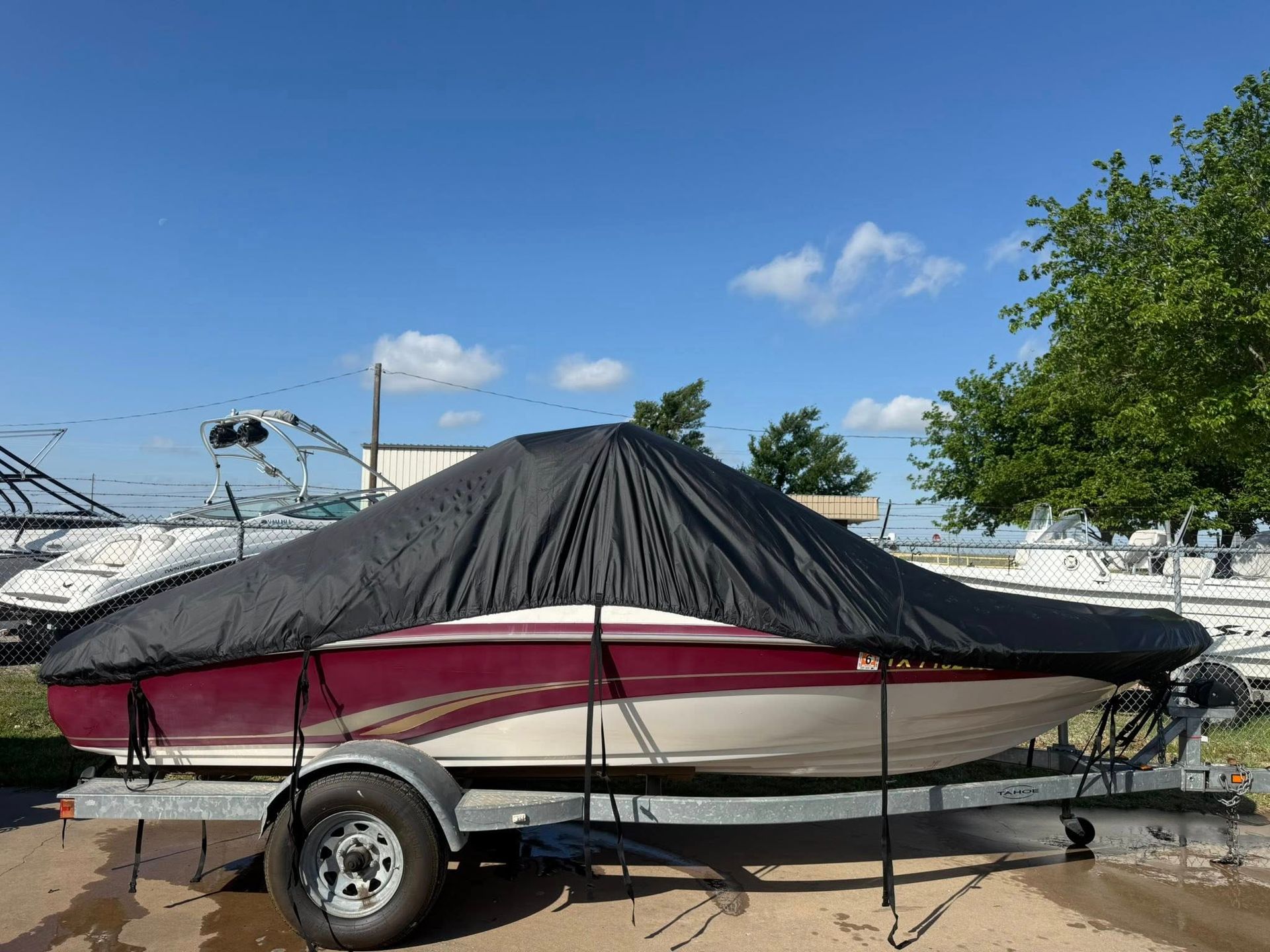 Covered boat on a trailer parked outdoors under a blue sky.