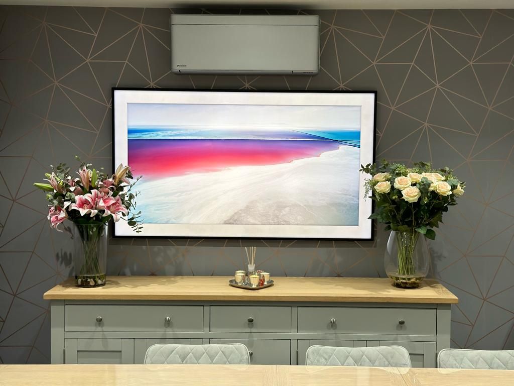 A picture of a beach is hanging on a wall above a dining table.