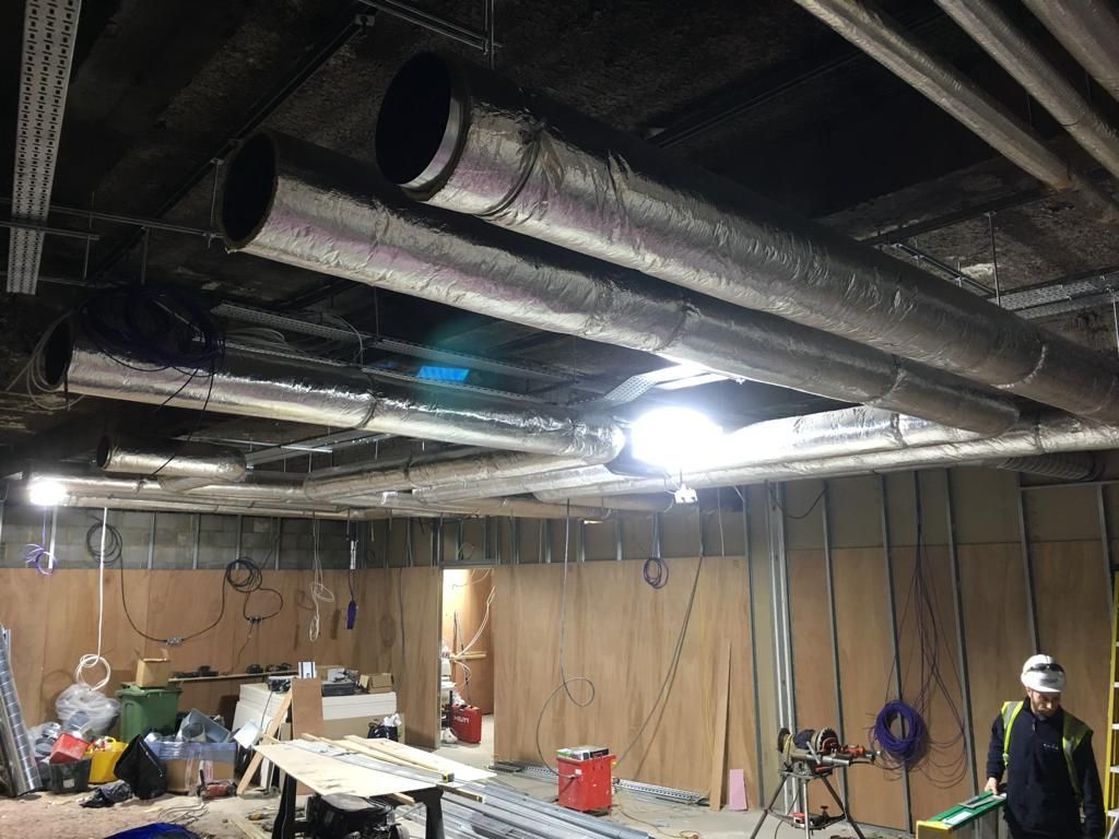 A man is standing in a room with a lot of pipes hanging from the ceiling.