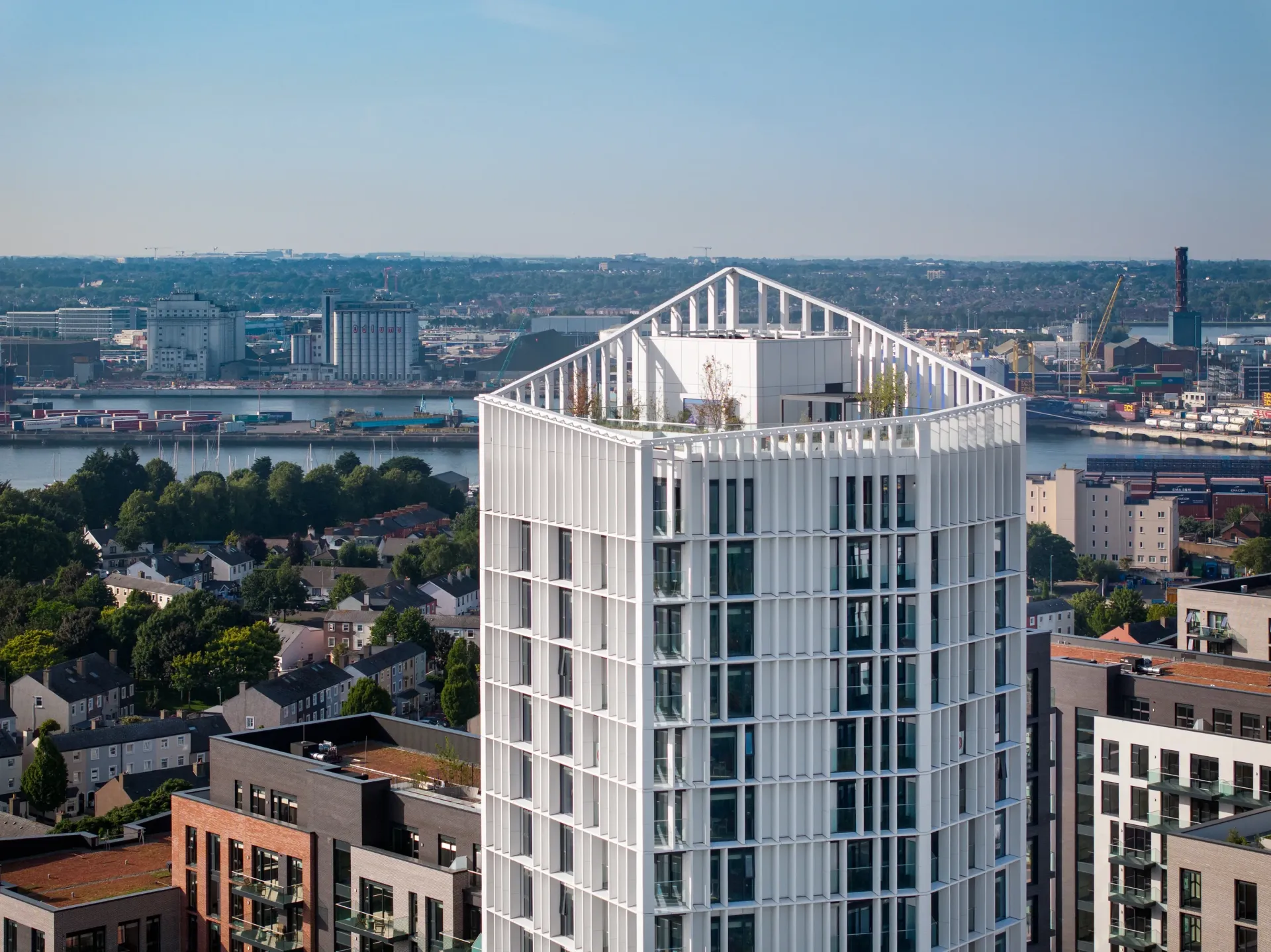 Aerial view of a white high-rise building with a pointed roof overlooking a city waterfront.