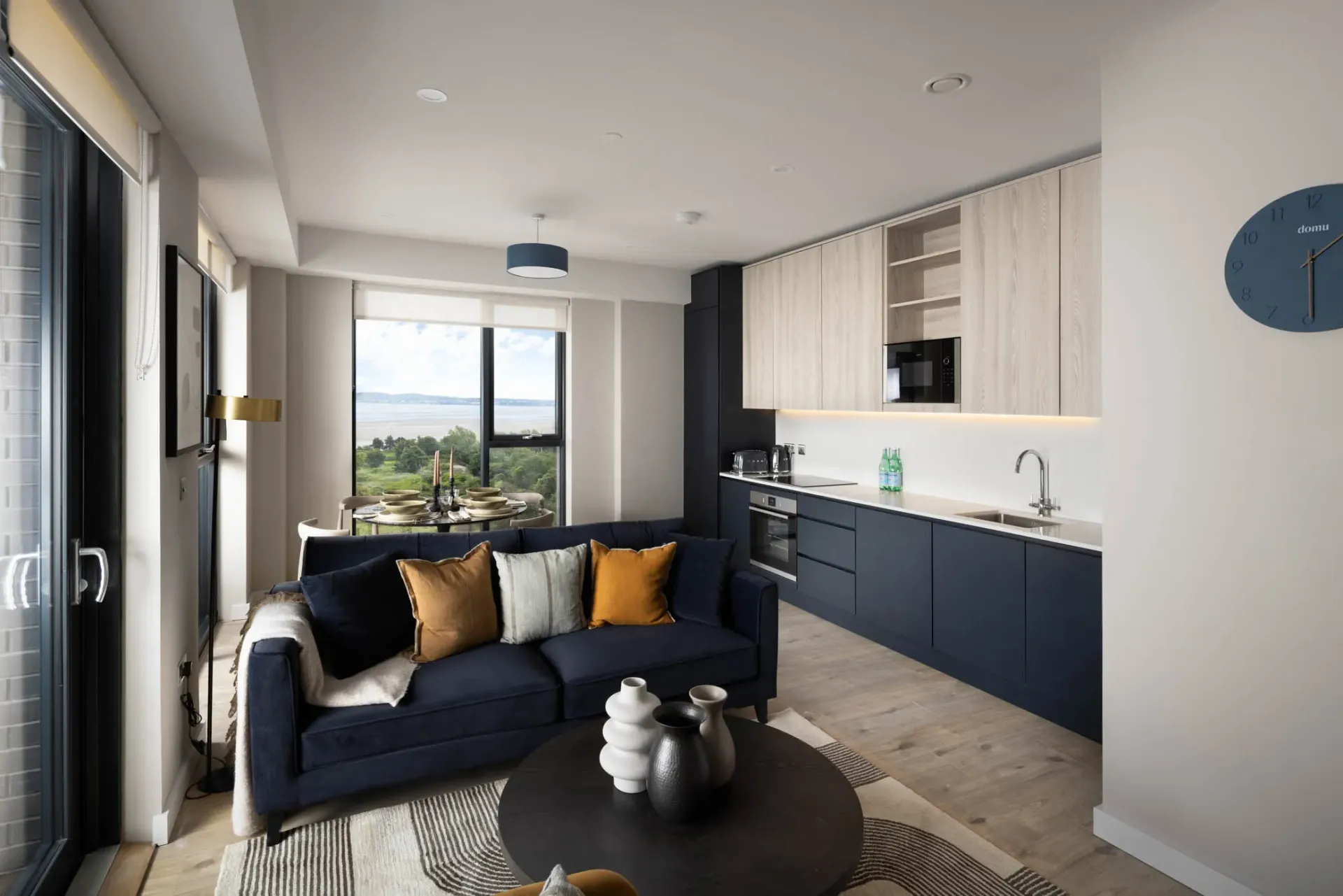 Modern living room with navy sofa, black coffee table, light wood cabinets, and city-view window