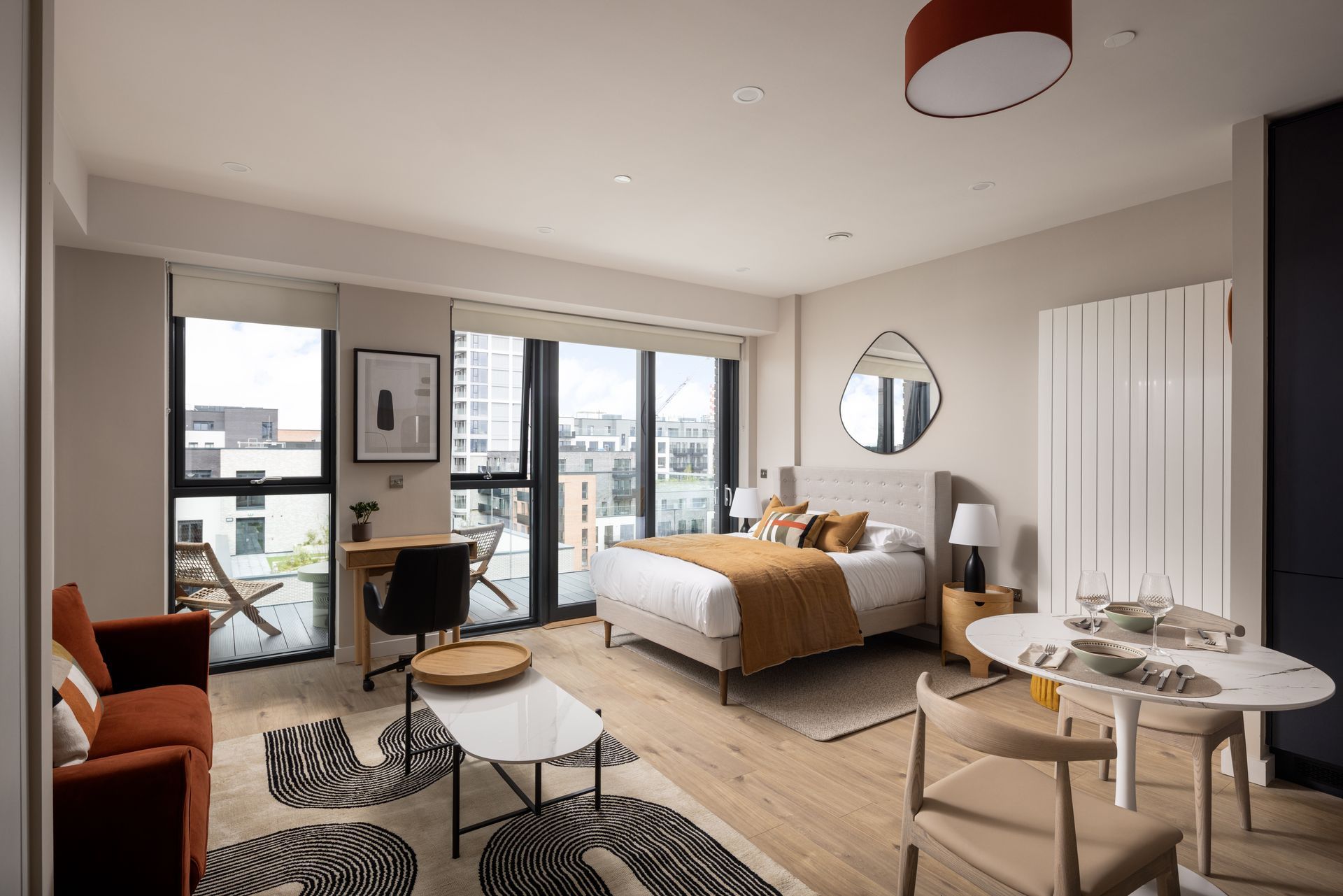 Modern studio apartment with bed, sofa, desk, and balcony doors in neutral tones