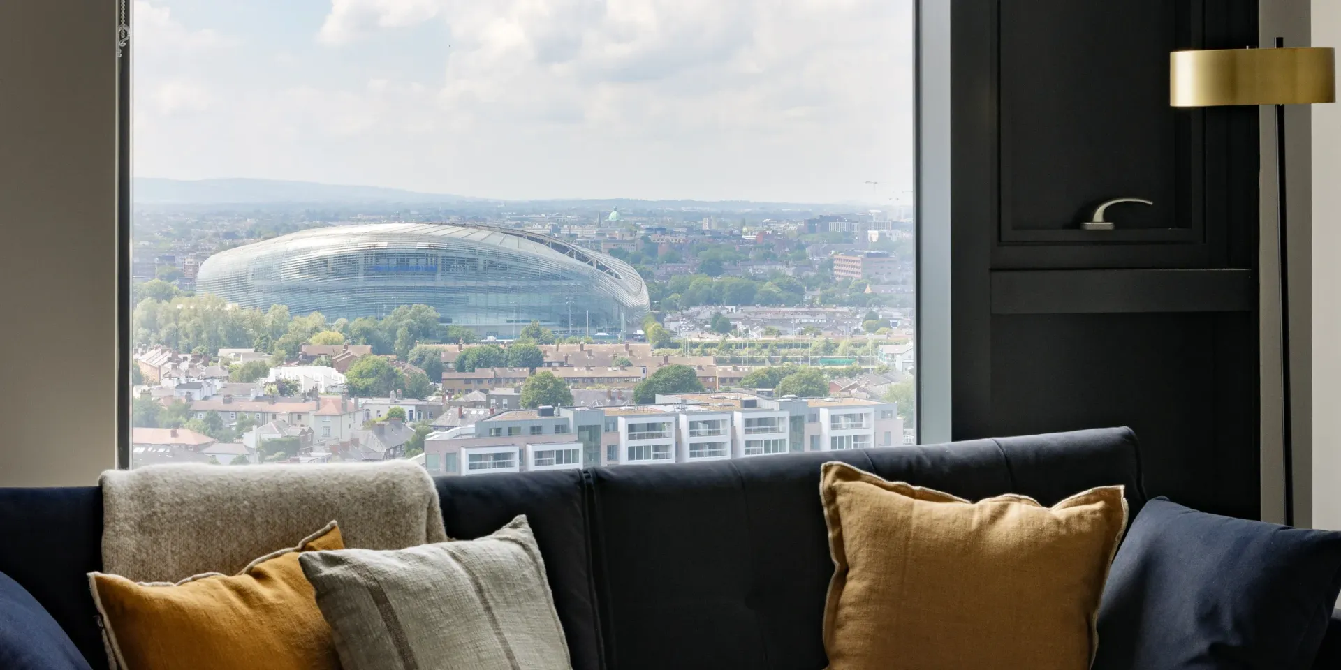 Modern living room window view over a city, with black and gold sofas and cushions in the foreground