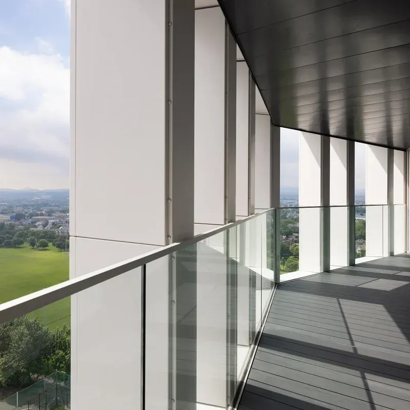 Modern balcony with glass railing and white columns overlooking green fields and distant city skyline
