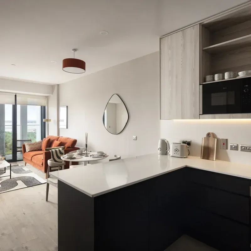 Modern open-plan living room and kitchen with black cabinets, white counters, orange sofa, and balcony view
