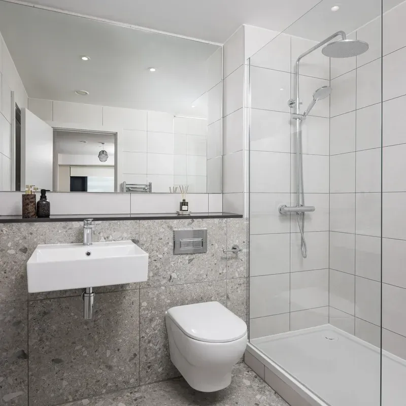 Modern white bathroom with wall-hung sink, toilet, large mirror, and glass shower enclosure