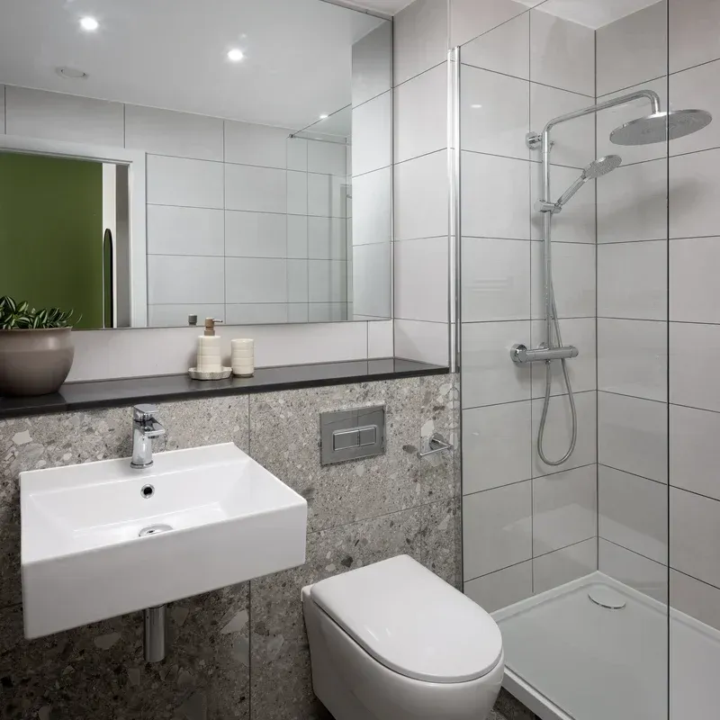 Modern white-tiled bathroom with wall-mounted sink, toilet, mirror, and glass shower enclosure