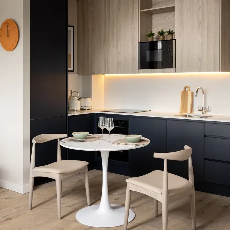 Modern kitchen with navy lower cabinets, light wood uppers, round white table, and two chairs