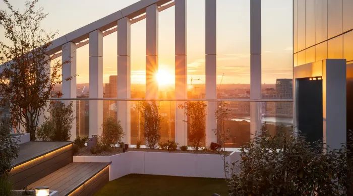 Sunset over a modern rooftop terrace with glass railings, plants, and city skyline views