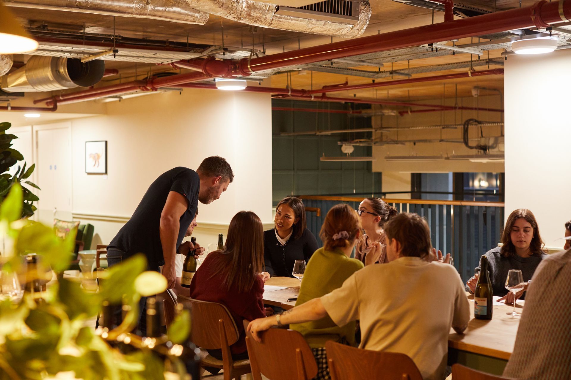 People seated at a table in a modern office, with a man leaning over to speak in a warm-lit meeting space