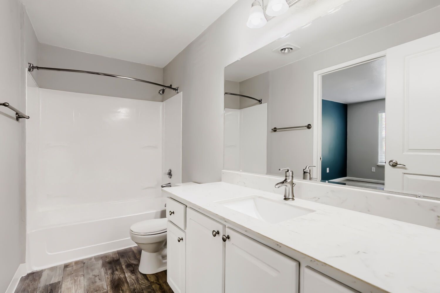 Bright white bathroom with tub-shower, toilet, vanity sink, and large mirror