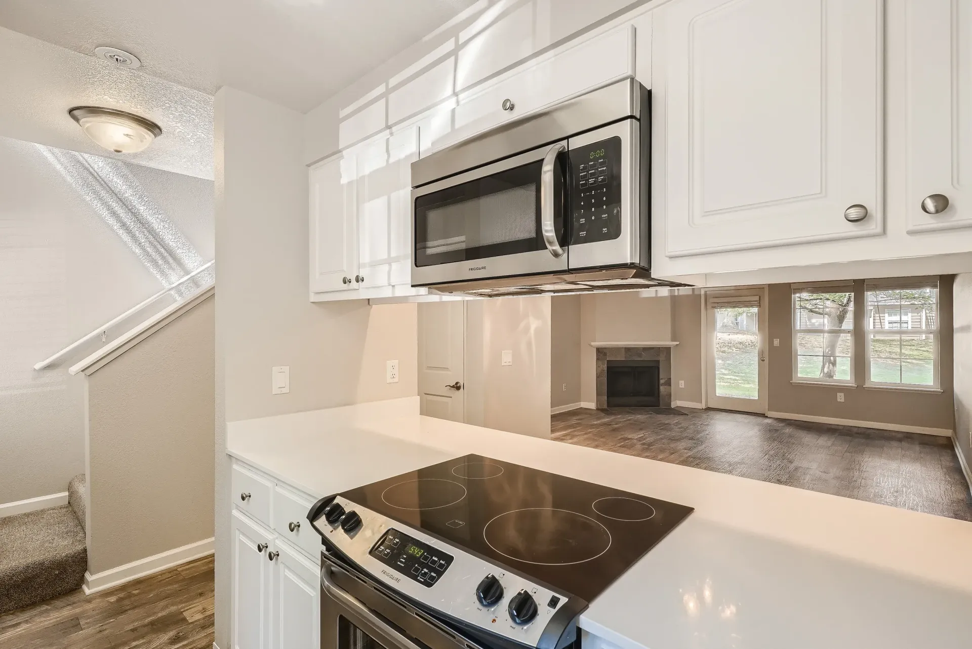 Kitchen with white cabinets, stainless microwave and stove, and a view into the living area with a fireplace.