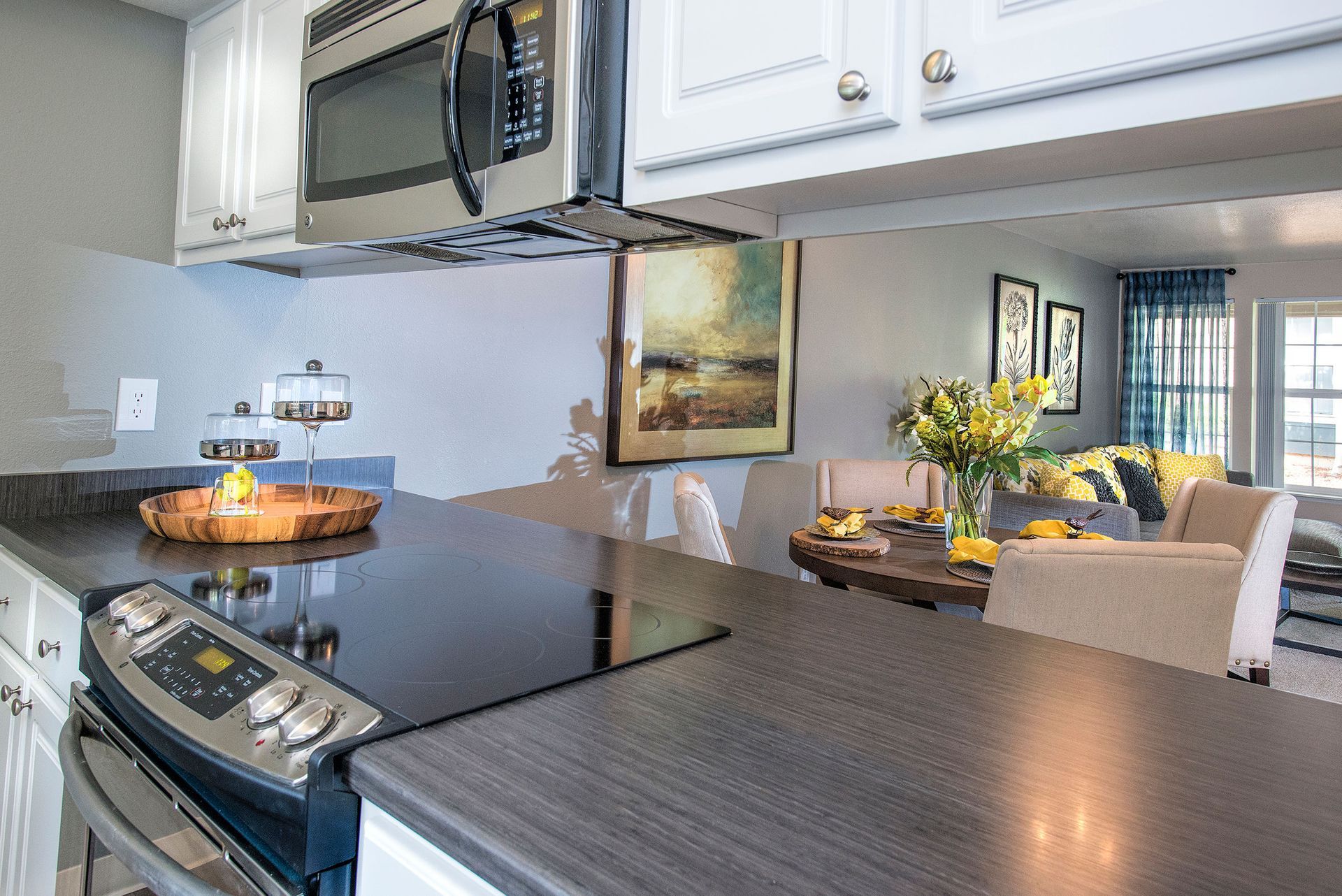 Open-concept kitchen with stainless steel microwave and stove; dining table and living area visible in background.