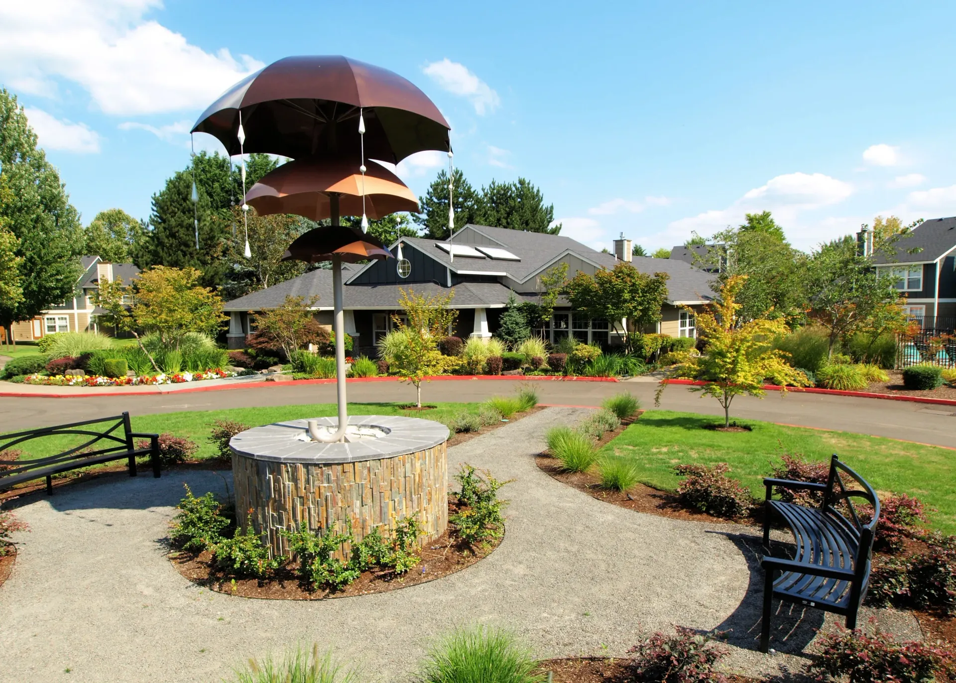 Outdoor community courtyard with benches, walkways, and decorative umbrellas beside apartment buildings.